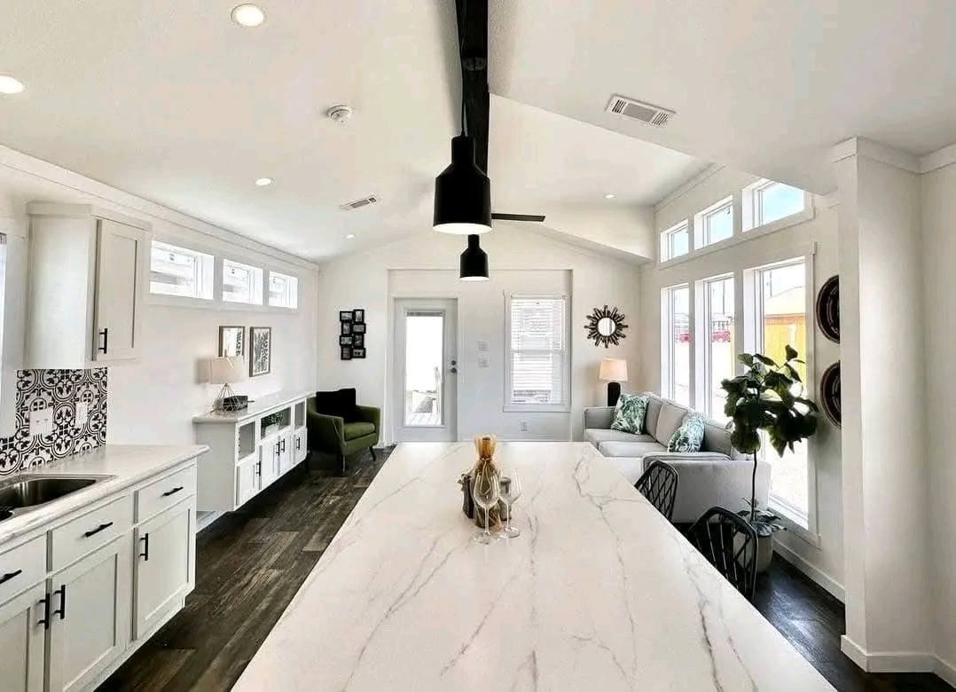 Modern open-concept living room with white walls, high ceilings, dark wood floors, large windows, and a kitchen island. Cozy seating area and contemporary decor.