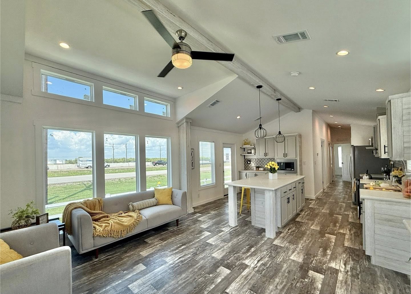 Bright modern living space with high ceilings, wood floors, and large windows. Includes a cozy sitting area, kitchen island, and pendant lights.