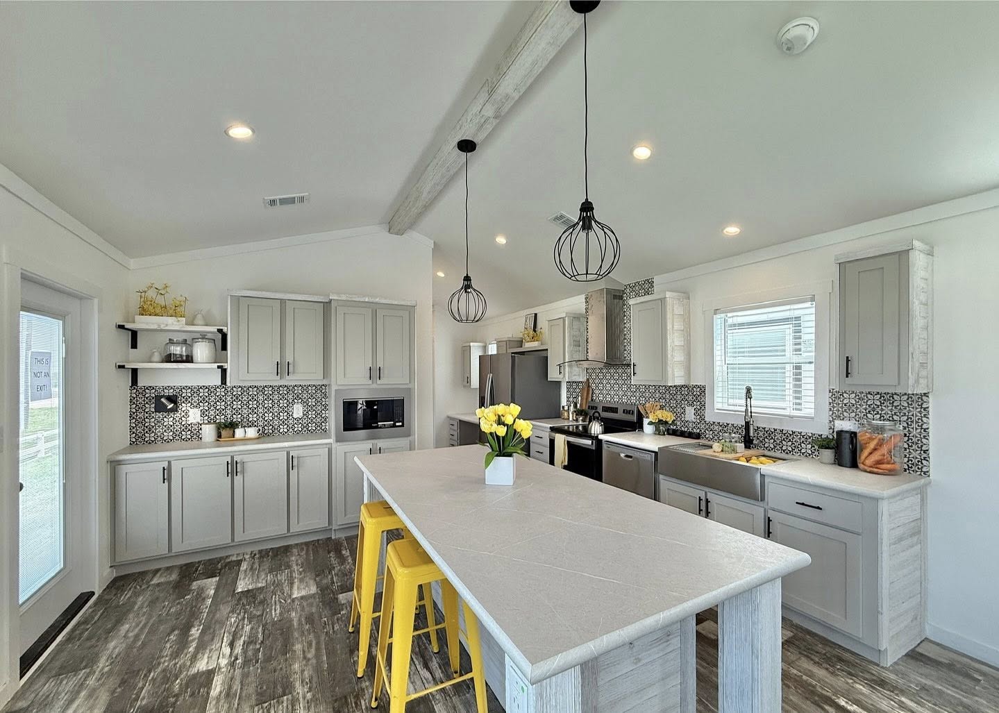 Modern kitchen with gray cabinets, a long island with bright yellow stools, pendant lights, and a vase of yellow flowers, creating a cheerful ambiance.