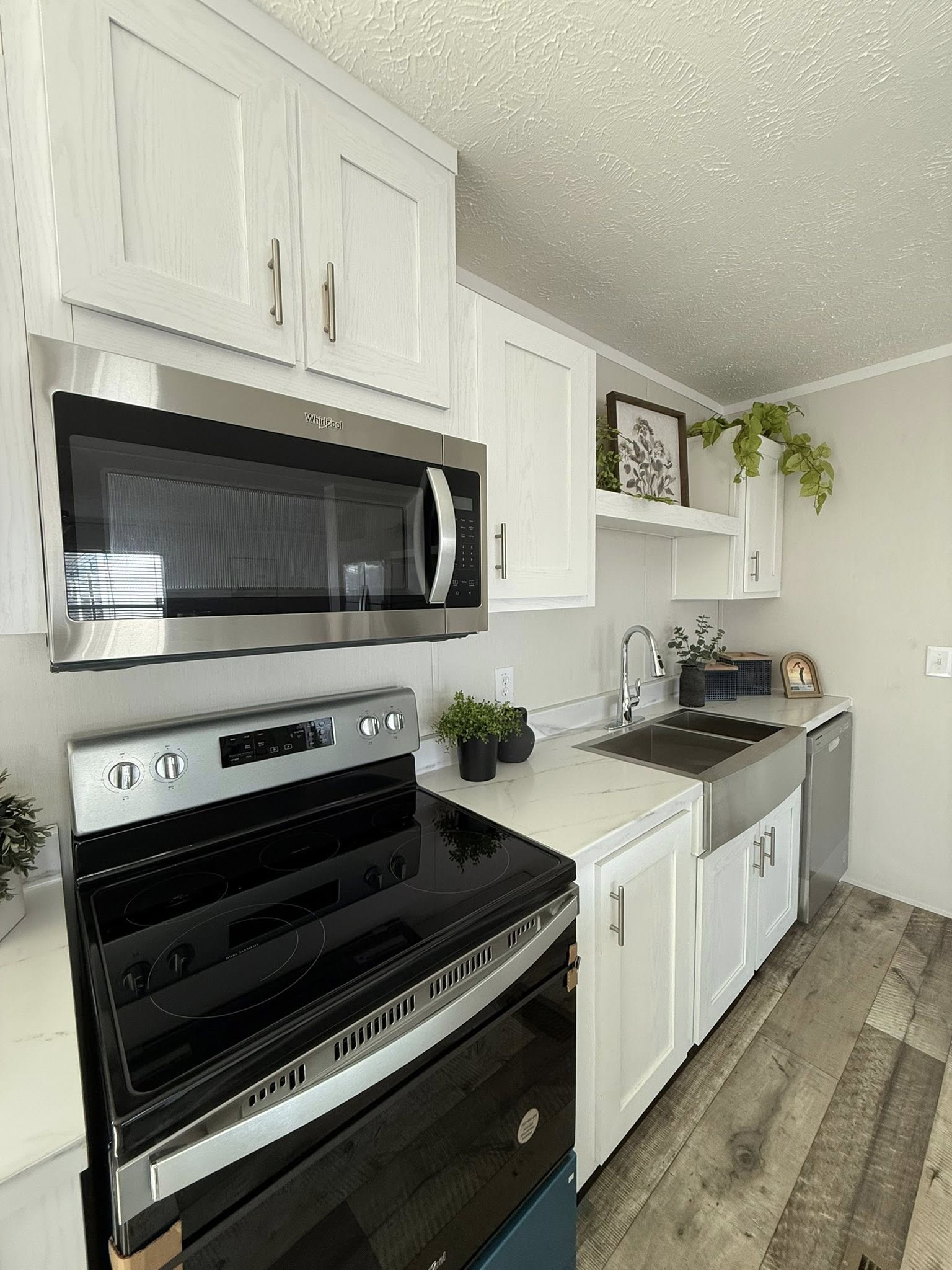 Modern kitchen with white cabinets, stainless steel appliances, and wood flooring. Plants and decor accent the clean, bright space, creating a cozy feel.