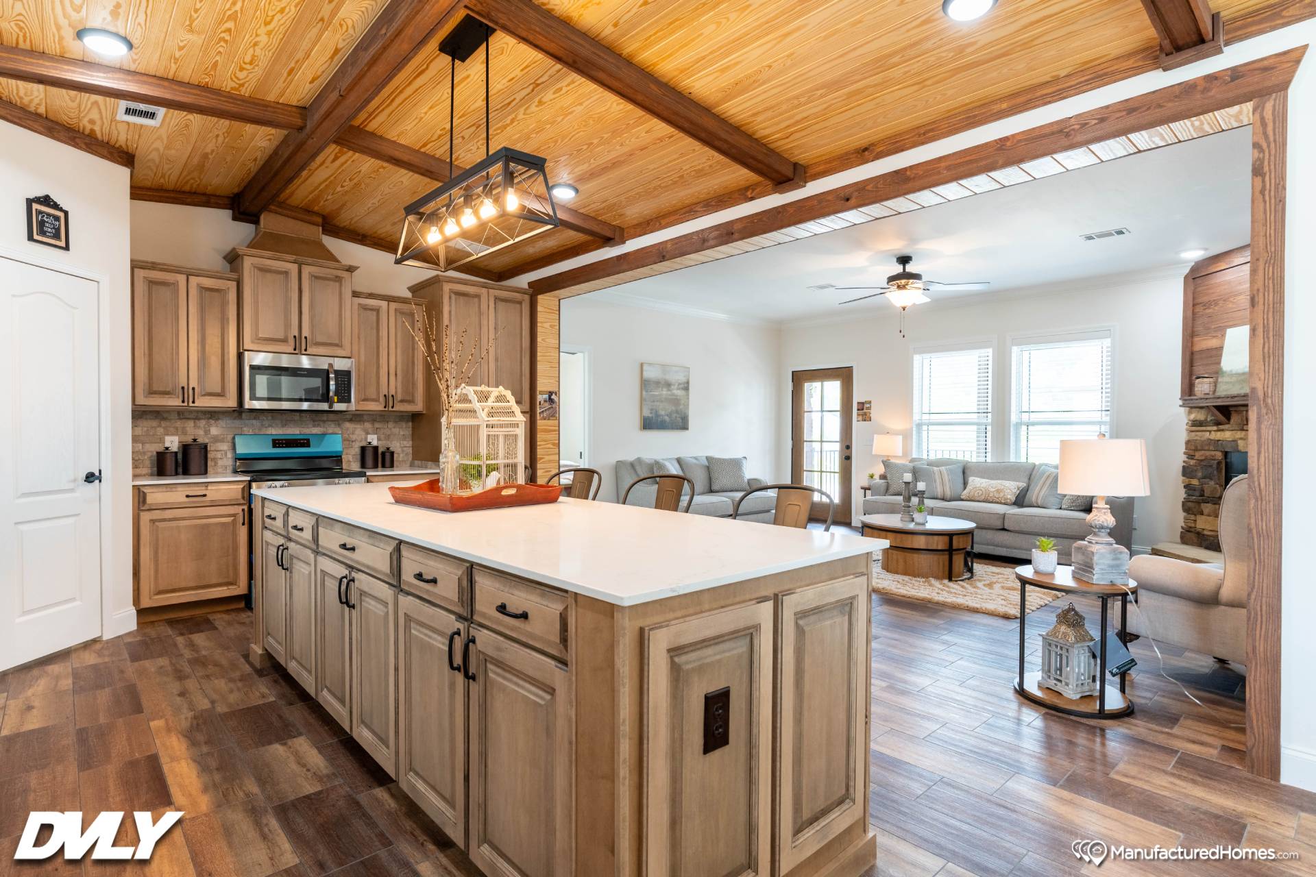 Spacious open-plan kitchen and living area. Kitchen features wooden cabinets, white island, and pendant lights. Cozy living room with neutral tones.