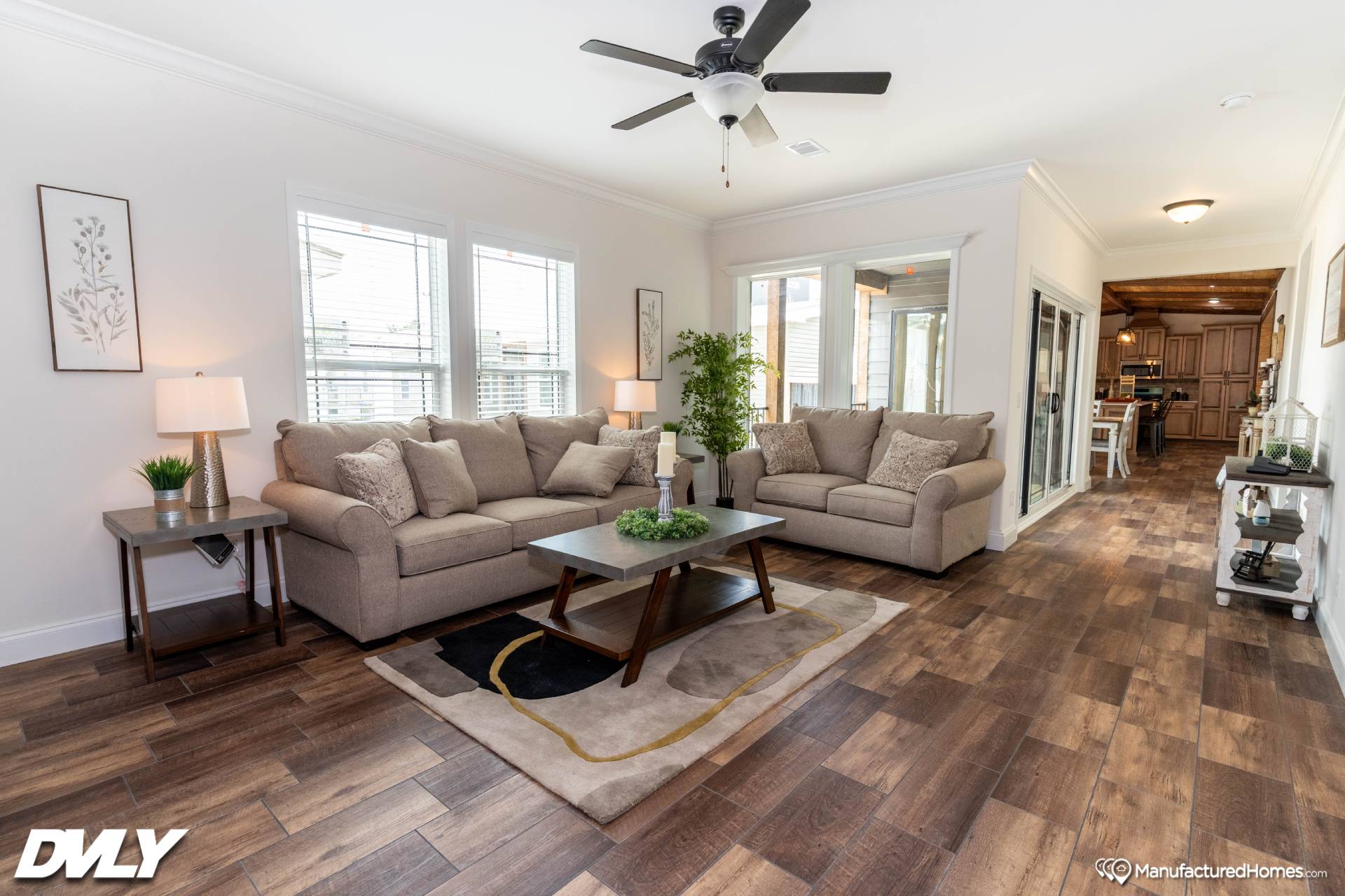 Modern living room with two beige sofas, a dark coffee table, and potted plant. Hardwood floors and a ceiling fan create a cozy atmosphere.