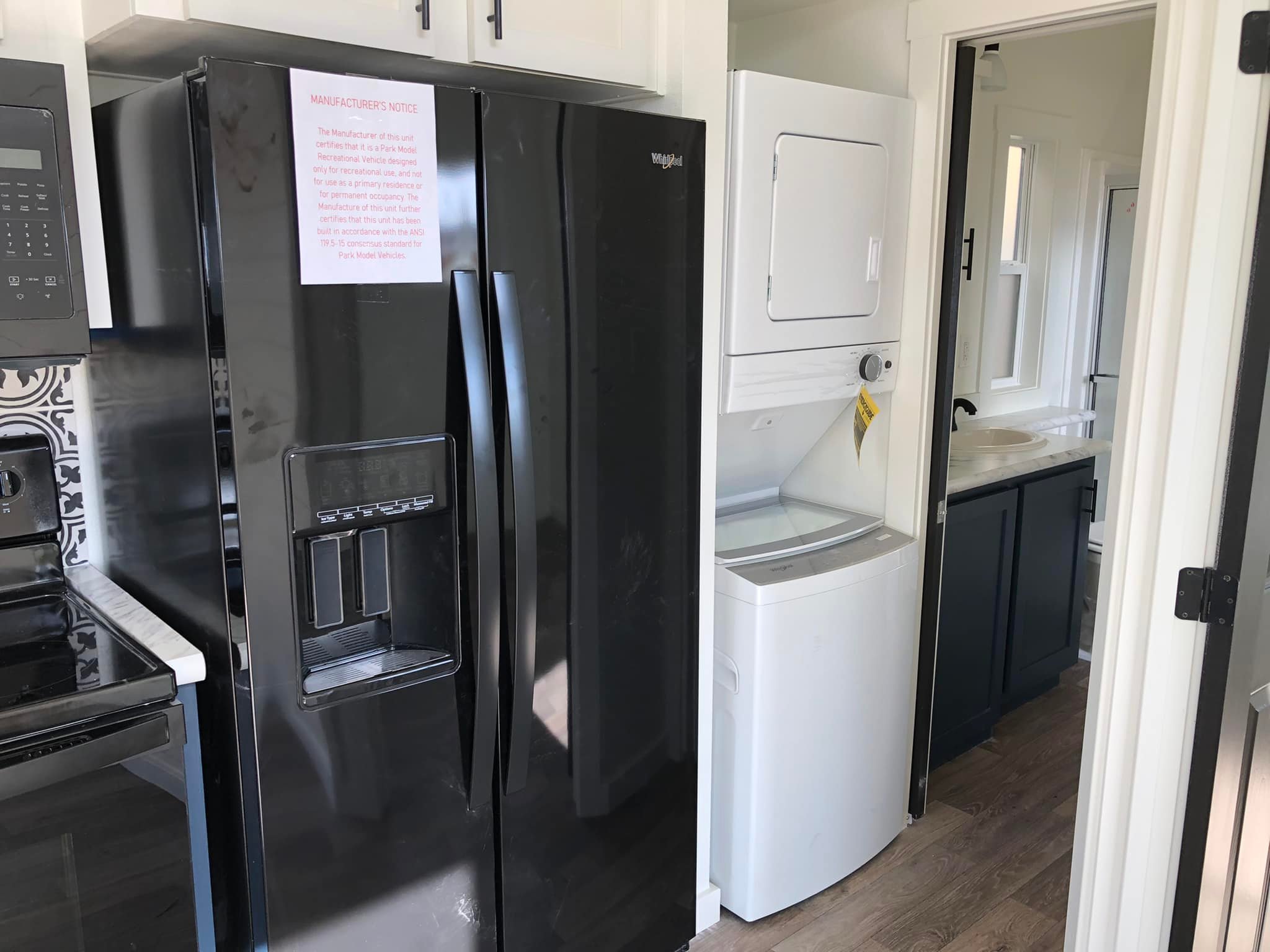 Compact kitchen and laundry area featuring a black refrigerator, stackable white washer and dryer, and a glimpse of a modern bathroom sink.