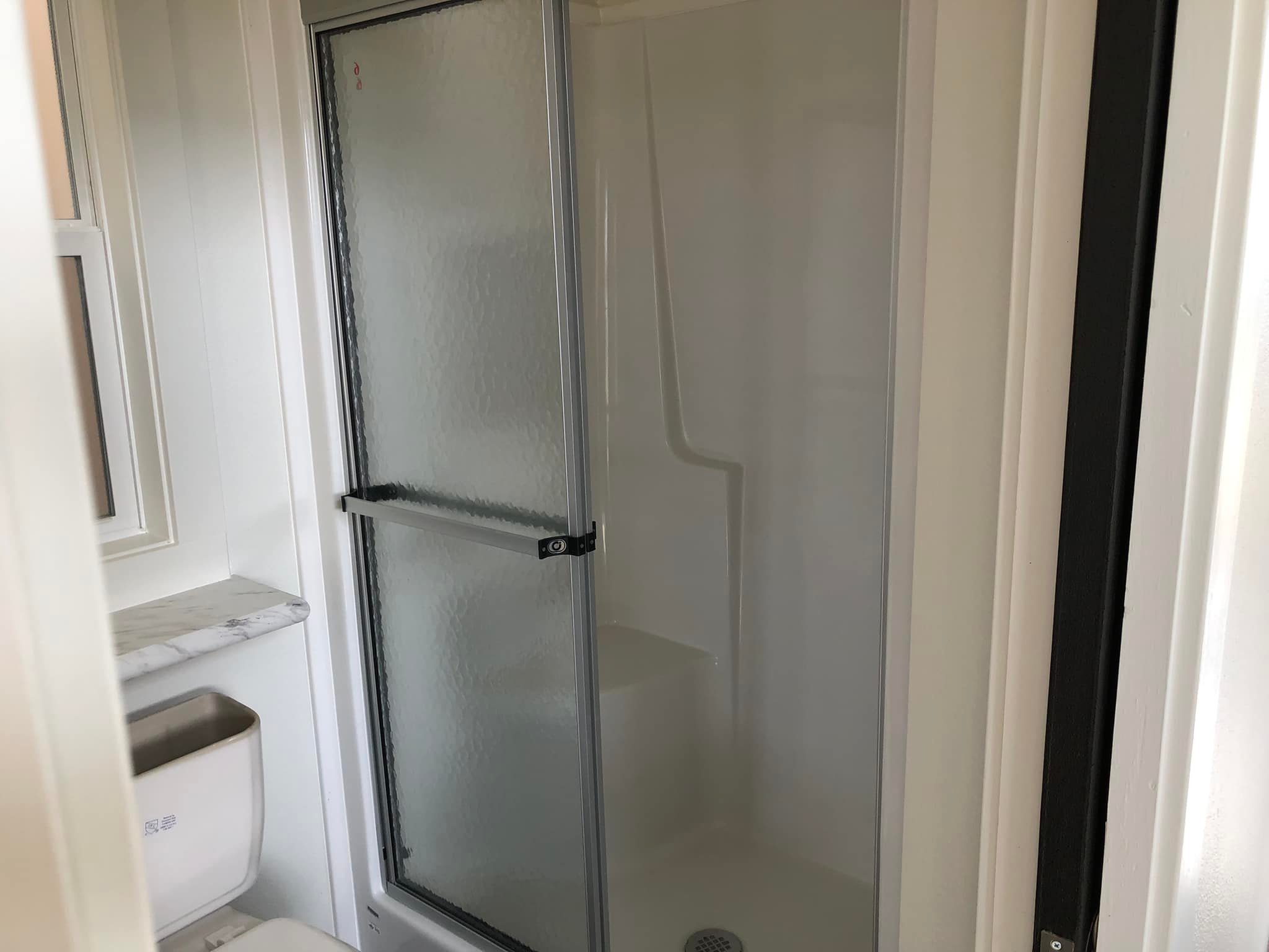 Compact bathroom with a frosted glass shower door, adjacent to a white toilet and marble countertop, creating a clean, simple atmosphere.