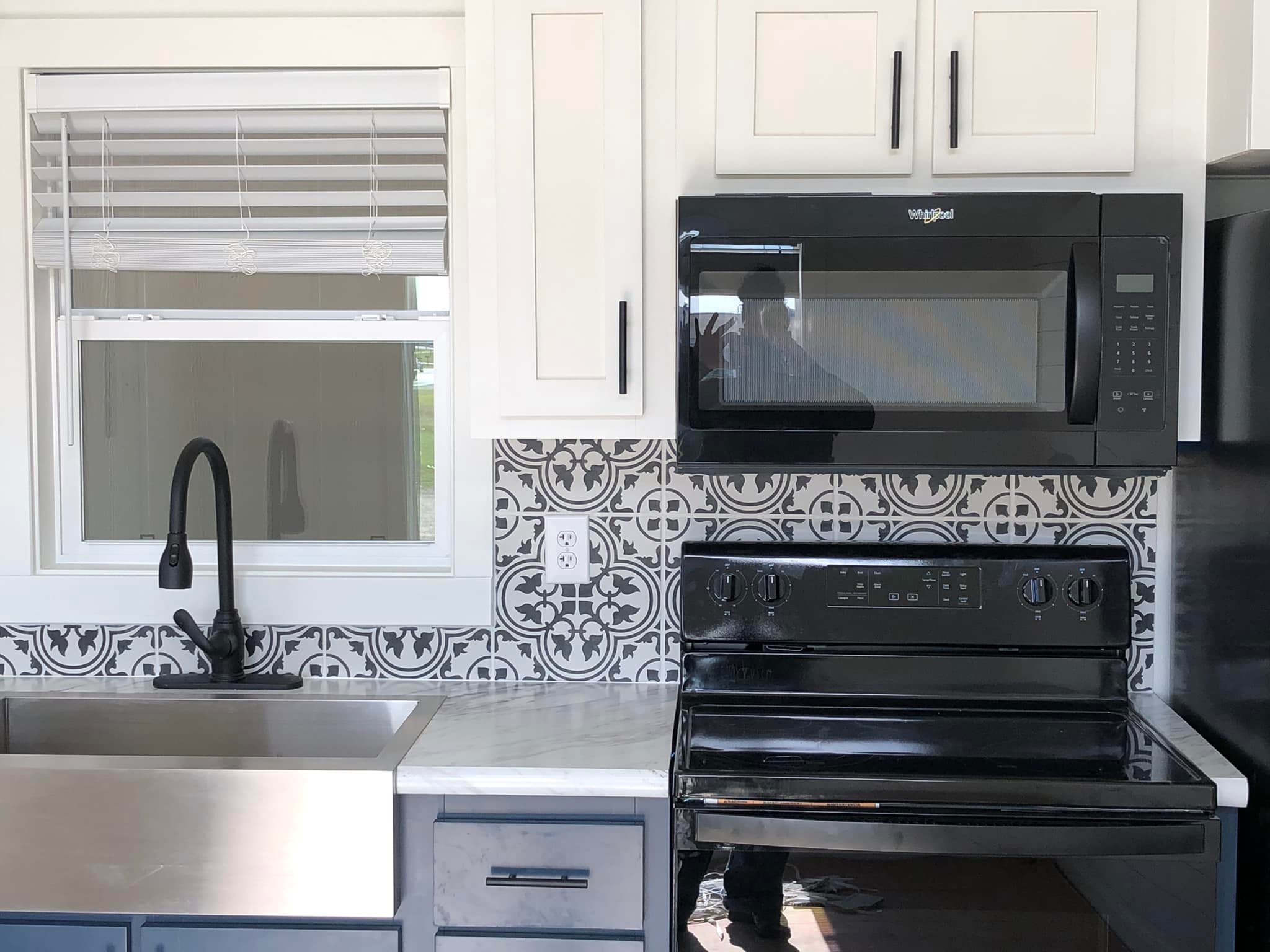 Modern kitchen with a black stove and microwave under white cabinets. A patterned gray backsplash adds contrast above the sink and counter.