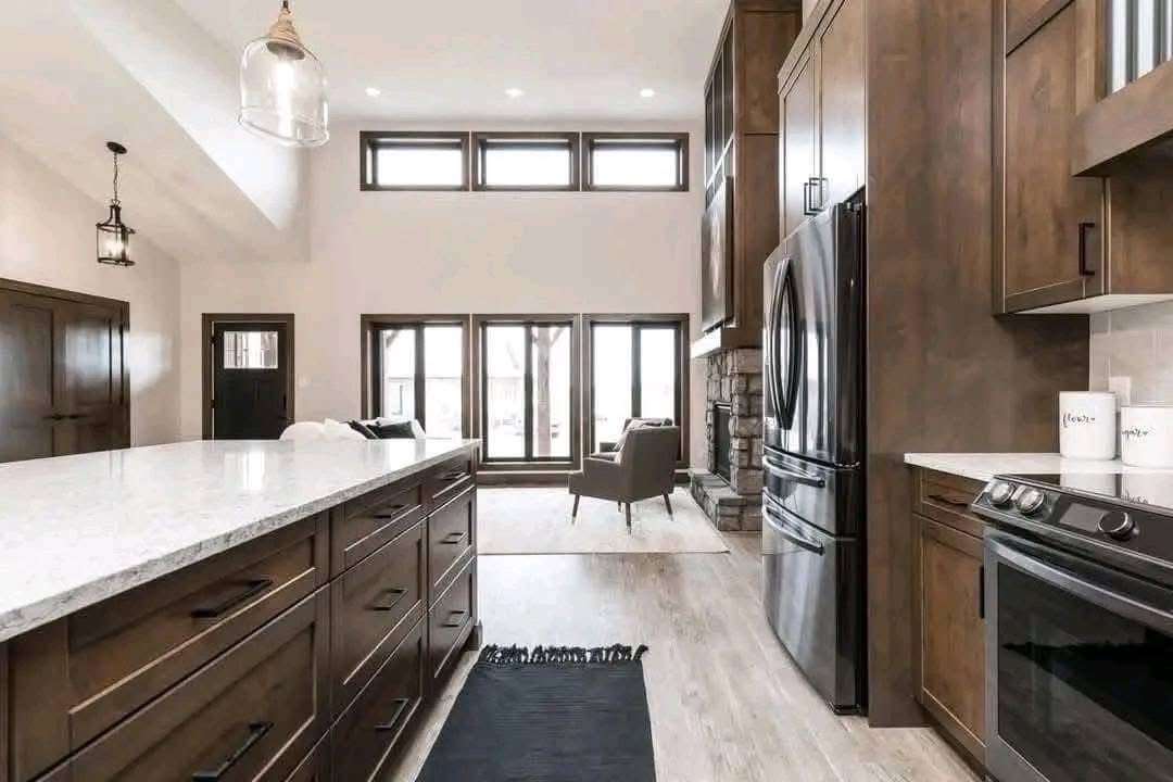 Spacious modern kitchen with high ceilings, wood cabinetry, and marble countertops. Large windows illuminate the airy space, creating a warm, inviting atmosphere.