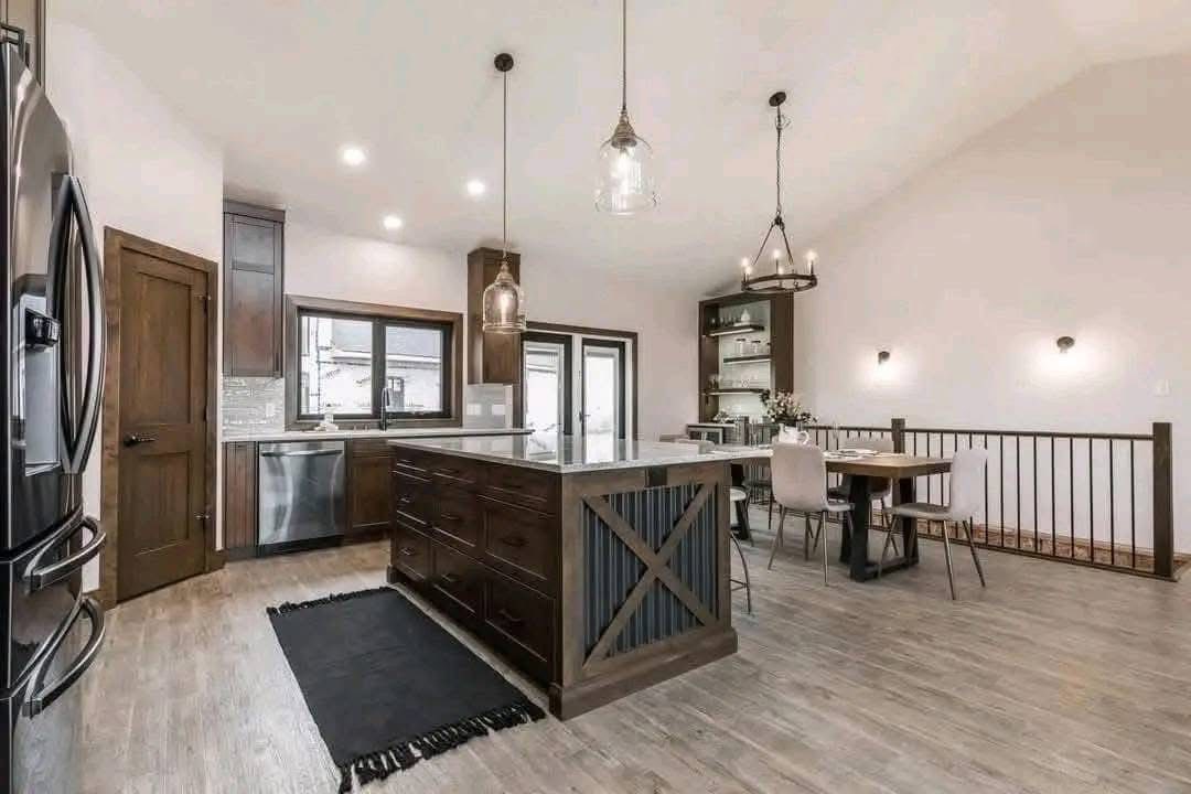 Spacious modern kitchen and dining area with light wood floors, a large island with dark wood cabinets, pendant lights, and a dining table with chairs.