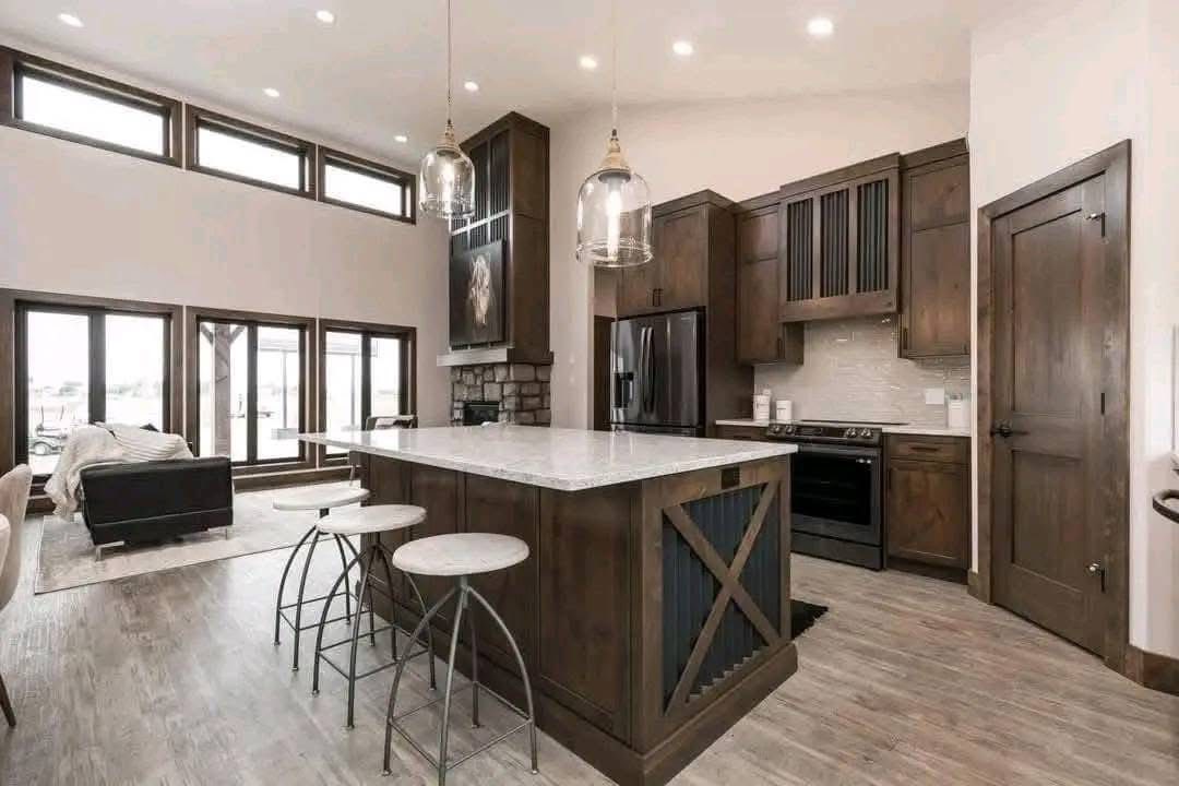 Modern kitchen with dark wood cabinets, a large island with stools, and pendant lights. Open layout connects to living area with a cozy sofa. Warm, inviting ambiance.