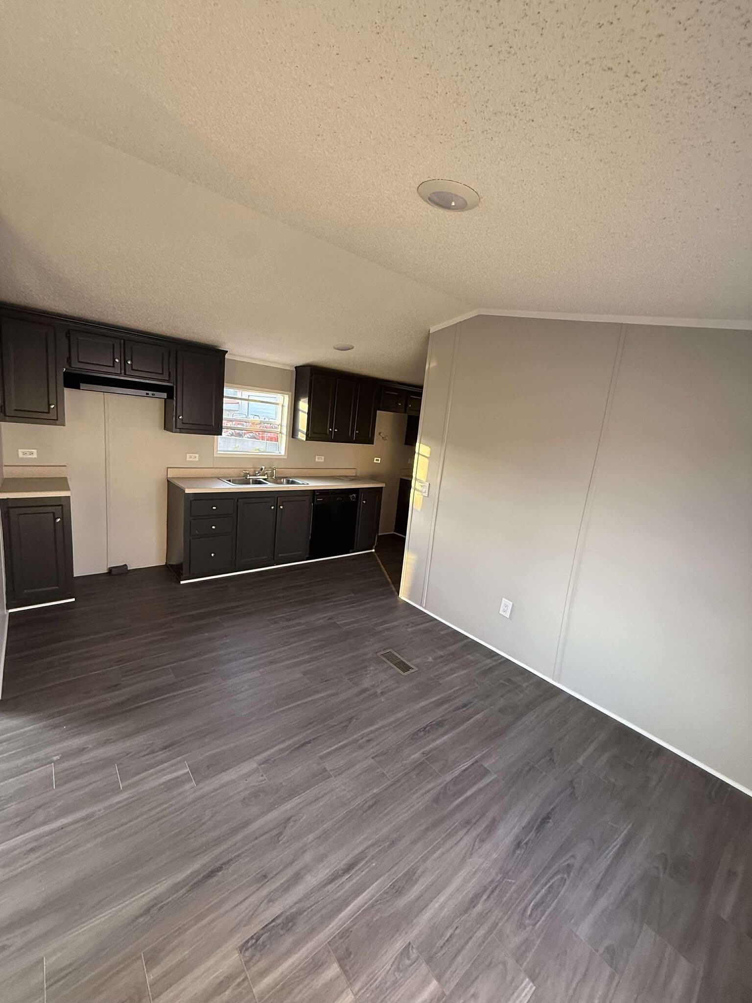 Modern, unfurnished kitchen with dark wood cabinets, a sink under a window, and light gray walls. The room has a clean, minimalistic feel.