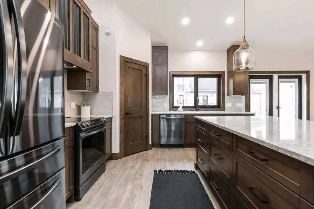 Modern kitchen with dark wood cabinets, stainless steel appliances, and a large island. Pendant light adds warmth, complementing the sleek design.