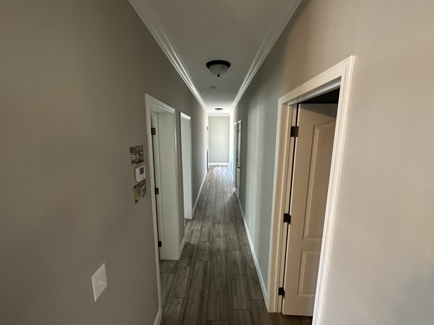 A bright hallway with light gray walls and wood-like flooring. Doors on either side lead to rooms. The space feels clean and spacious.