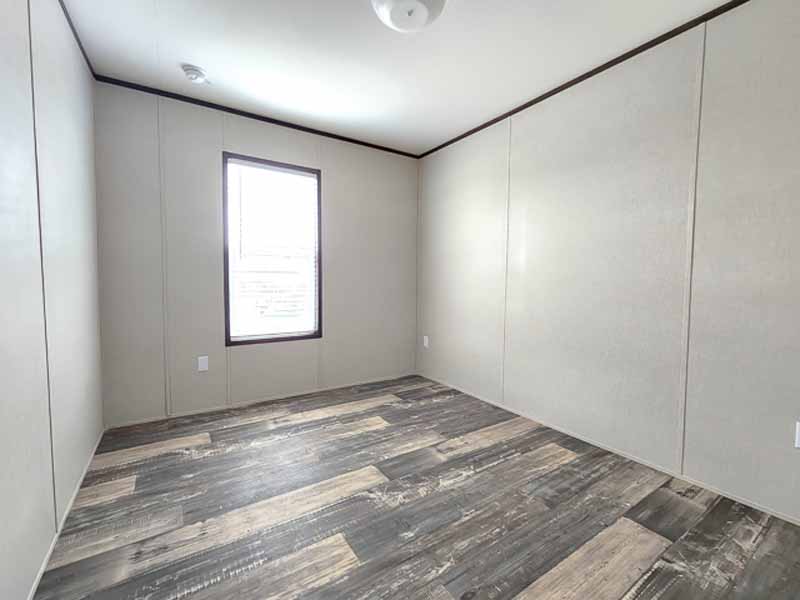 Empty room with beige walls and weathered wood flooring. A single window lets in light, creating a clean, minimalist, and neutral atmosphere.
