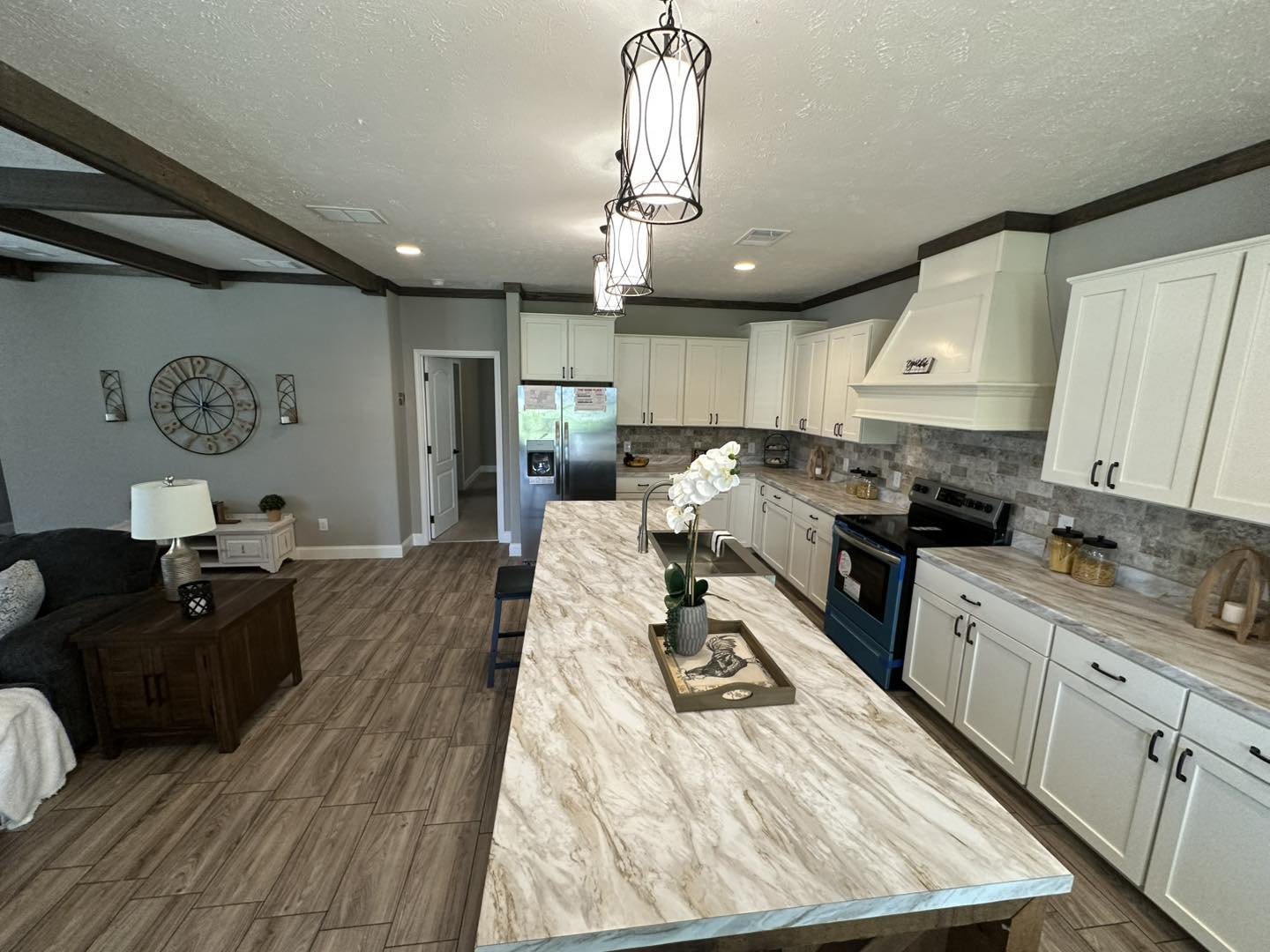 Spacious kitchen with white cabinets and a long marble island featuring a decorative tray and potted plant. Pendant lights hang above, creating a cozy ambiance.