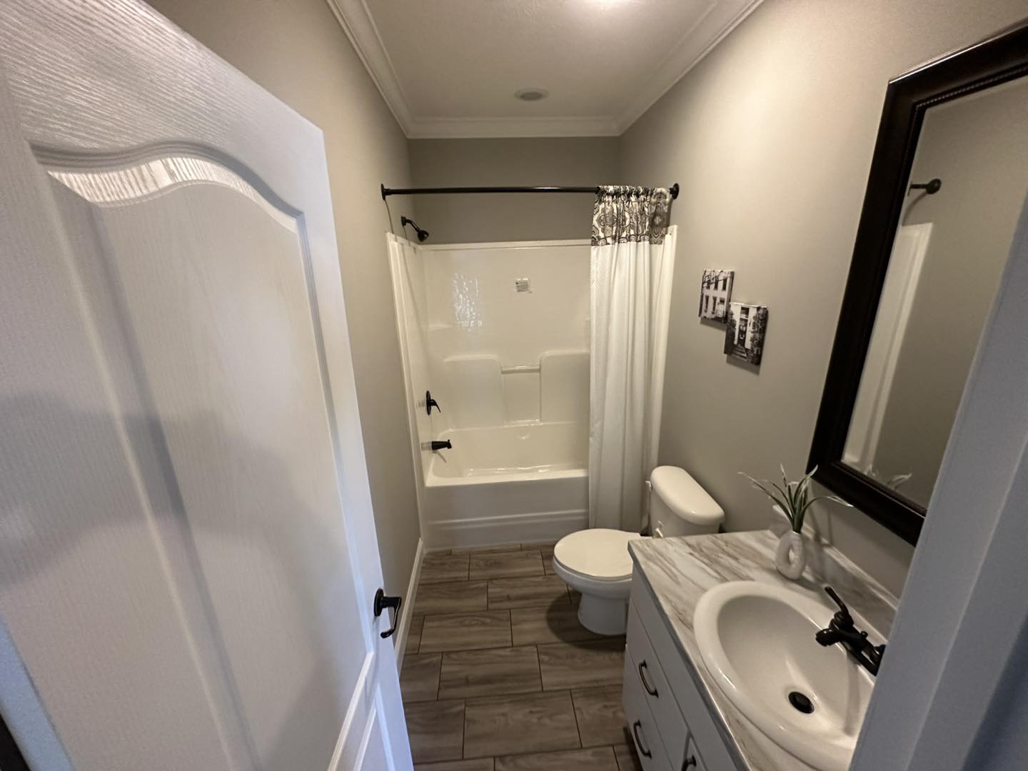 Modern bathroom with a gray and white color scheme. Features a marble countertop vanity, rectangular bathtub, large mirror, and wood-look tile floor.