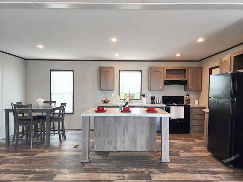 Modern kitchen with wood floors, central island, red dishes, and black appliances. Dining table with chairs on the left, bright and inviting.
