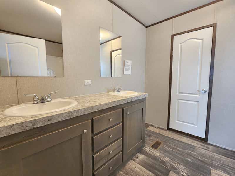 A modern bathroom features a dual sink vanity with a marble countertop, two mirrors, and a closed white door. The floor has a wooden finish.