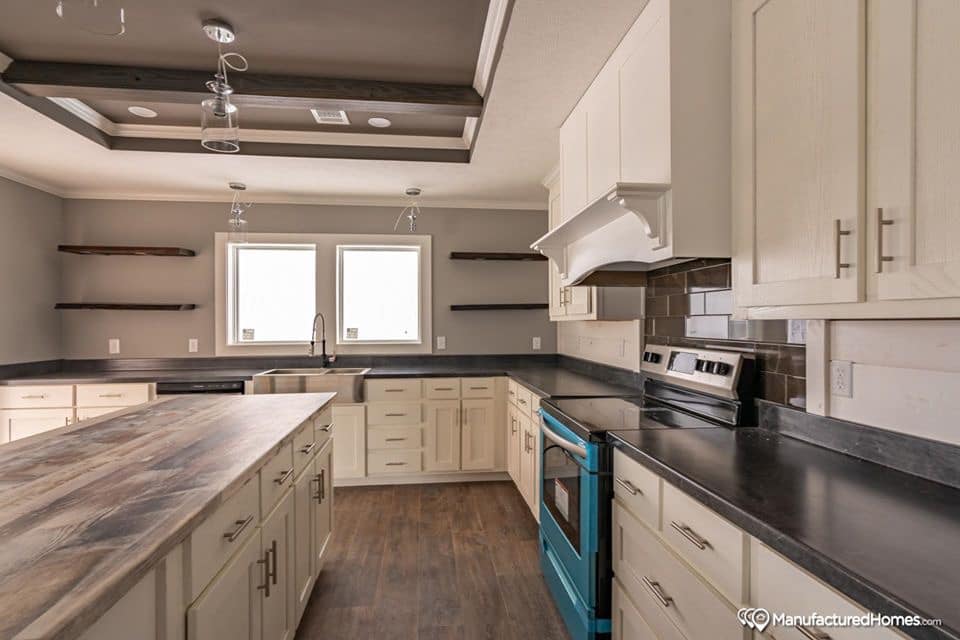 Spacious modern kitchen with wooden floors, white cabinets, dark countertops, and a large island. Two windows brighten the room, creating an inviting ambiance.