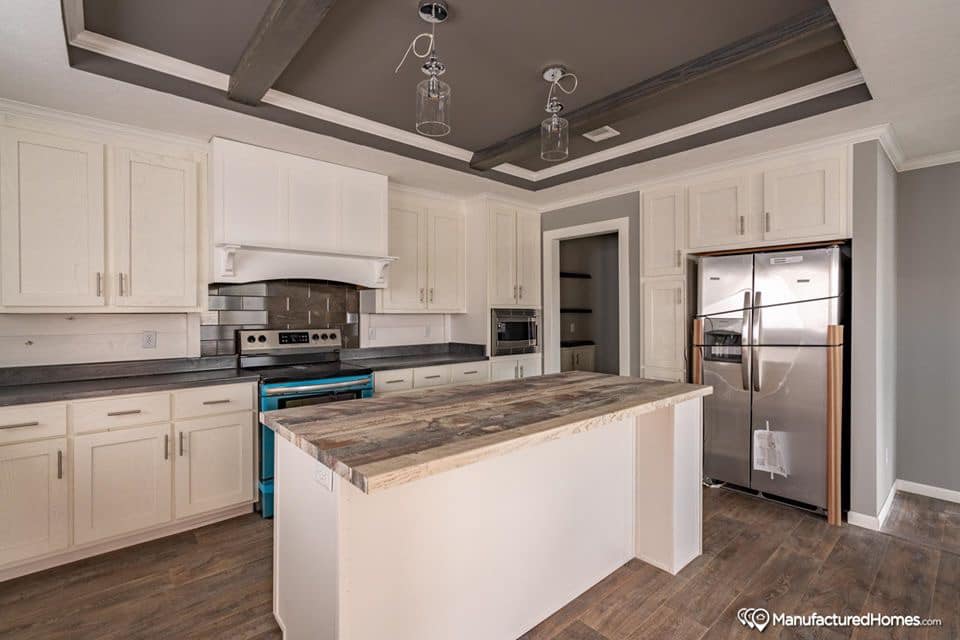 Spacious modern kitchen with wooden floors, white cabinets, dark countertops, and a large island. Two windows brighten the room, creating an inviting ambiance.