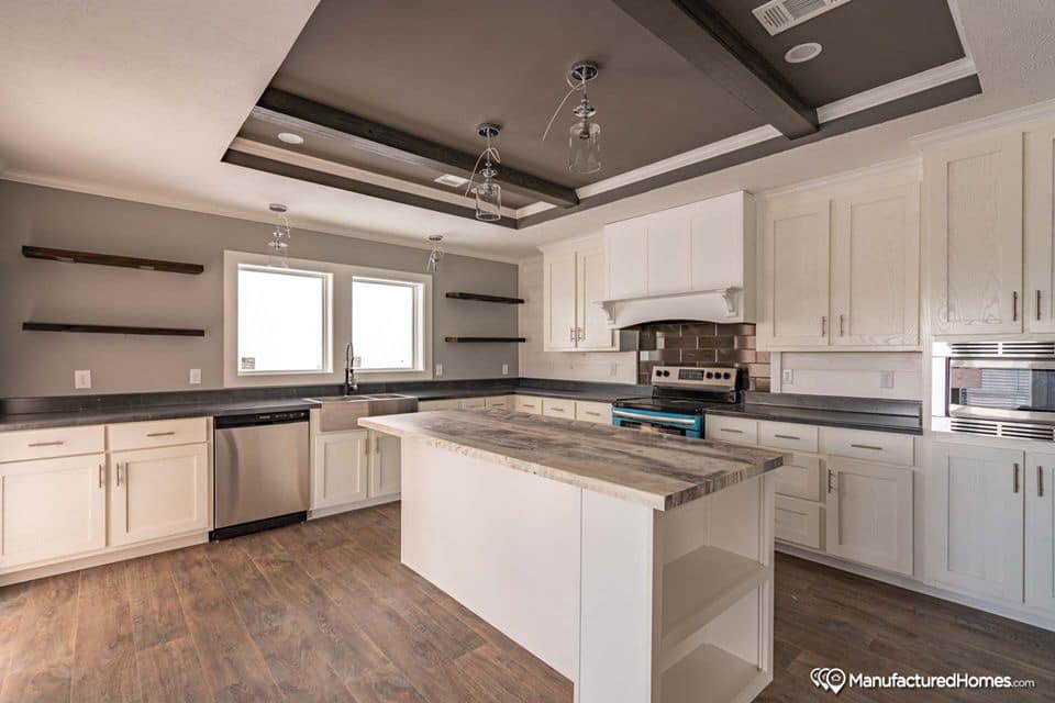 Modern kitchen with white cabinets, a large wooden island, and stainless steel appliances. Floating shelves and sleek lighting create a stylish, airy feel.