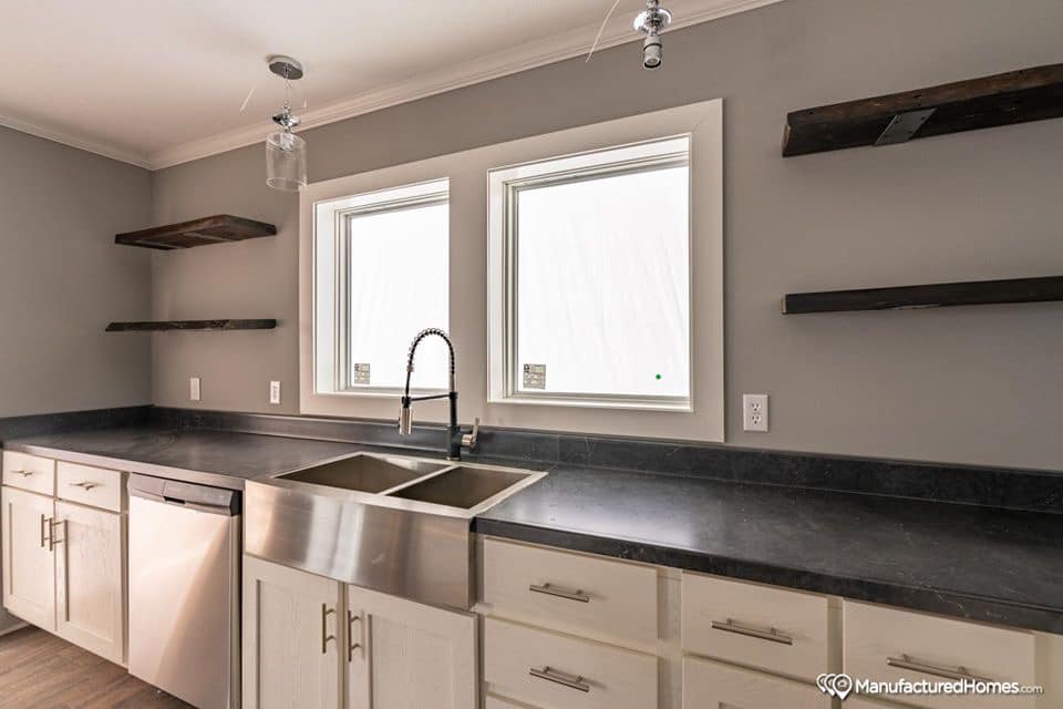Modern kitchen with gray walls, dark countertops, and a stainless steel double sink. Shelves flank two windows, creating a minimalist, airy feel.
