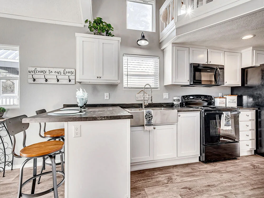 Modern kitchen with white cabinets, black appliances, and a farmhouse sink. Natural light from windows and door. Cozy and welcoming ambiance.