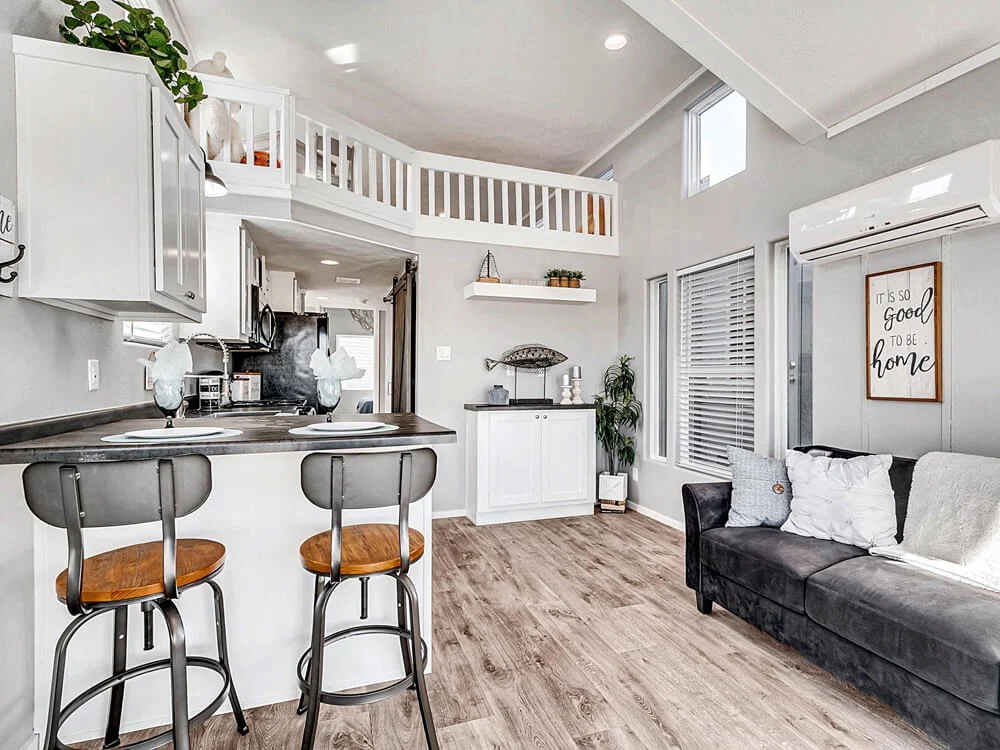 Modern tiny home interior with high ceilings, featuring a cozy kitchen area with bar seating, loft, and a welcoming living space with a black sofa.