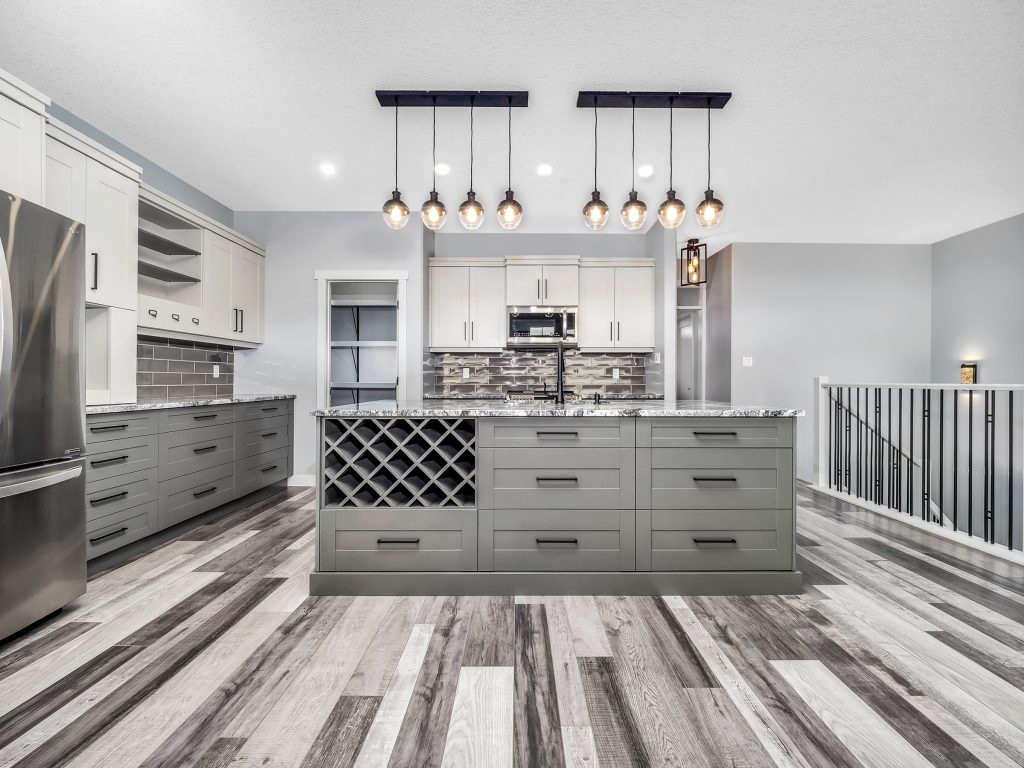 Modern kitchen with a large island featuring a built-in wine rack, sleek gray cabinets, stainless steel appliances, and pendant lighting. Stylish and spacious.