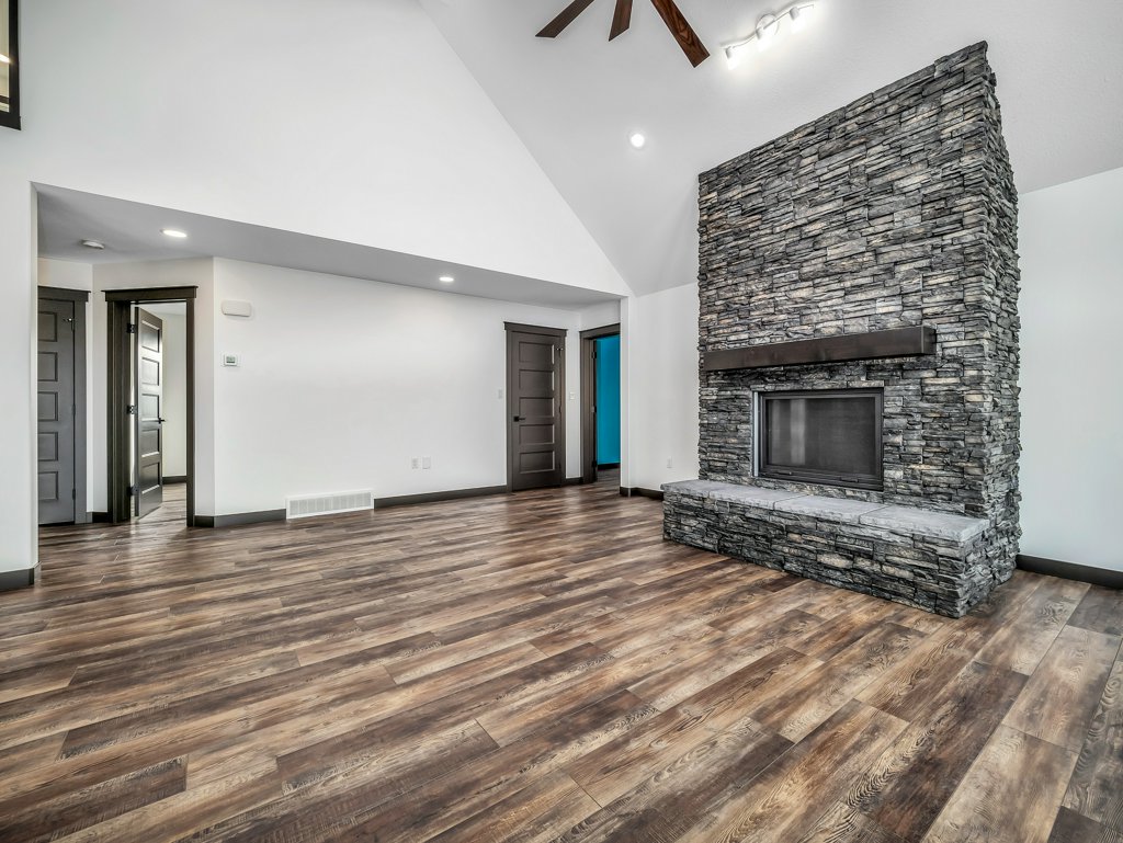 Spacious living room with a vaulted ceiling, dark wood flooring, and a large stone fireplace. The neutral walls and open layout create a warm, inviting ambiance.