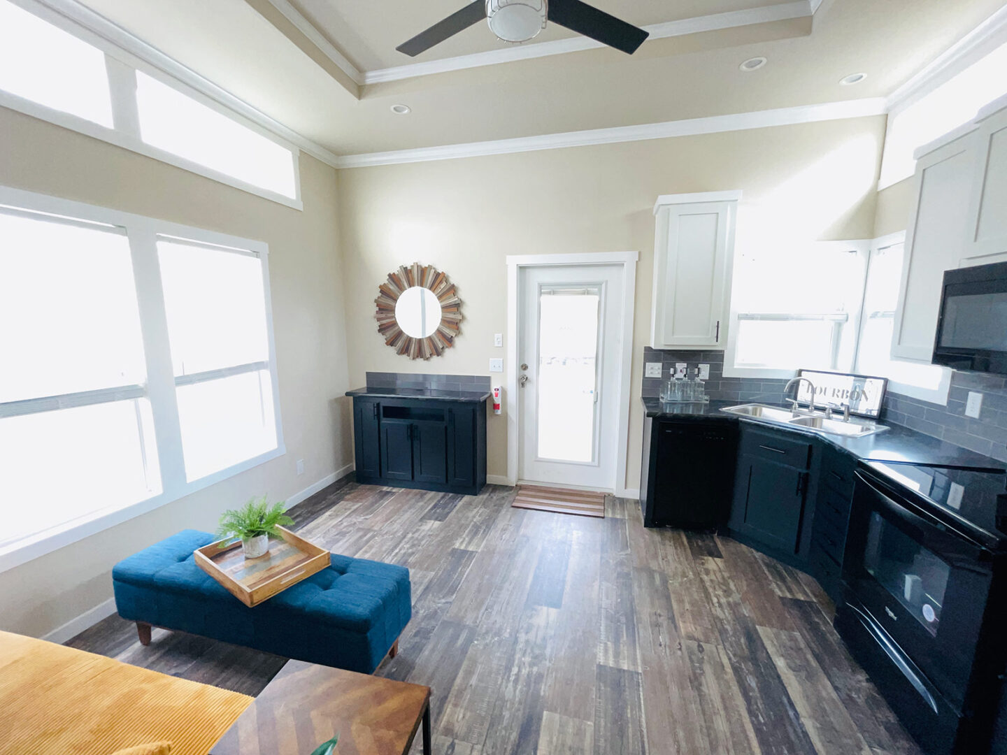 Modern kitchen with light walls, dark cabinetry, and wood flooring. A round mirror hangs near a glass door. Bright, spacious, and inviting atmosphere.