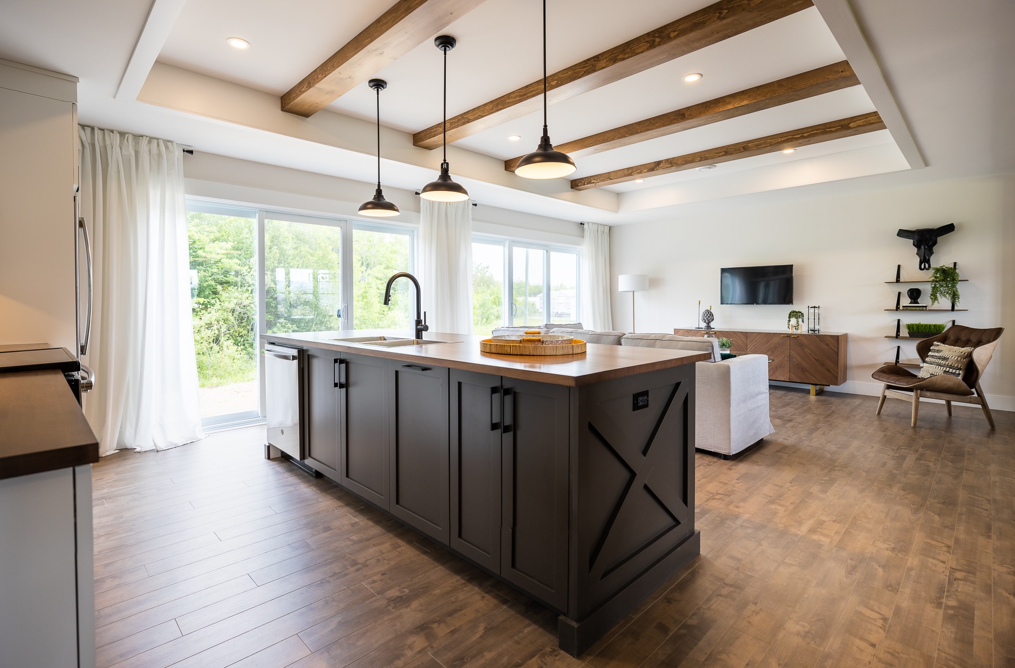 Modern kitchen with a wooden island, pendant lights, and hardwood floors. Bright with natural light from large windows. Cozy, open, and inviting.
