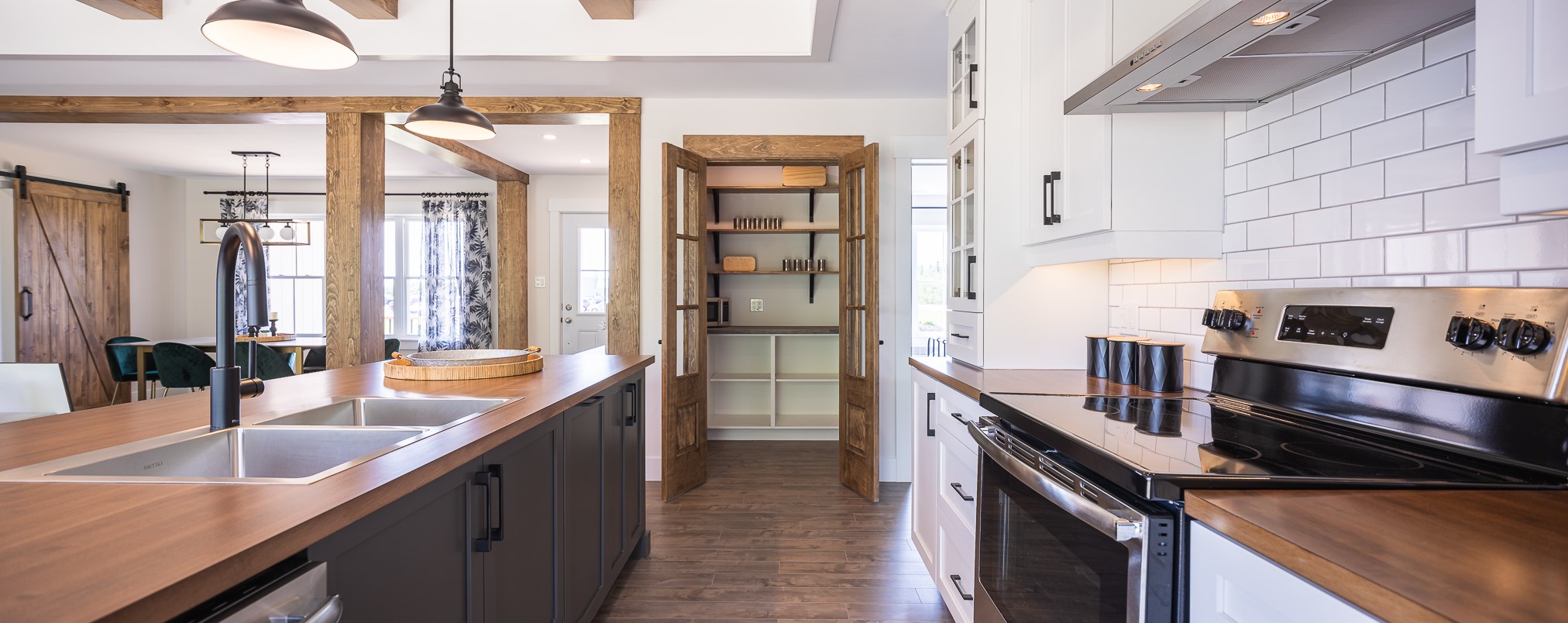 Modern kitchen with white cabinets, stainless steel appliances, and wooden countertops. An open pantry with shelves is visible. Bright and inviting.