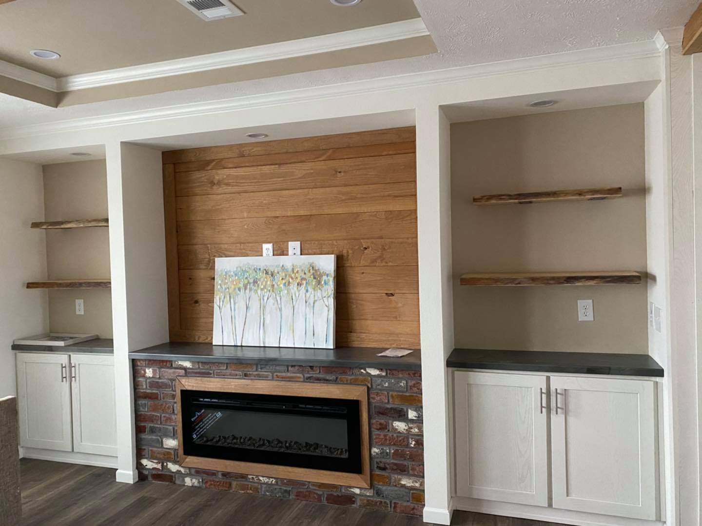 Modern living room with a central brick fireplace, flanked by built-in shelves and cabinets. A painting rests above, evoking a calm, cozy vibe.