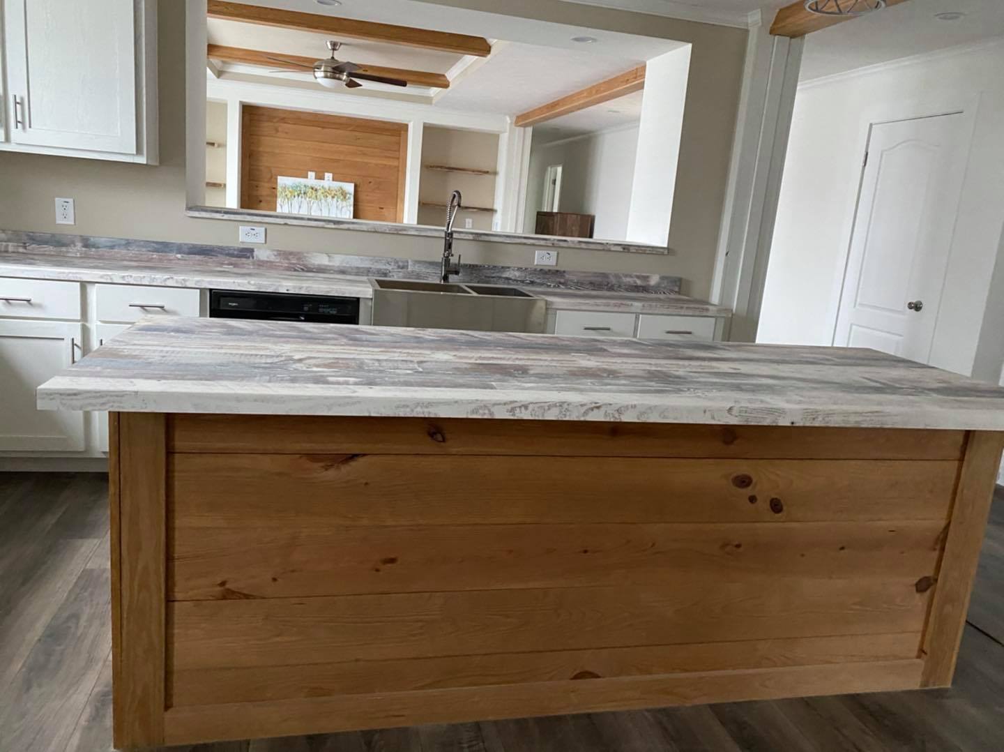 Rustic kitchen with a large wooden island topped with distressed marble. White cabinetry and a farmhouse sink enhance the cozy, modern farmhouse vibe.