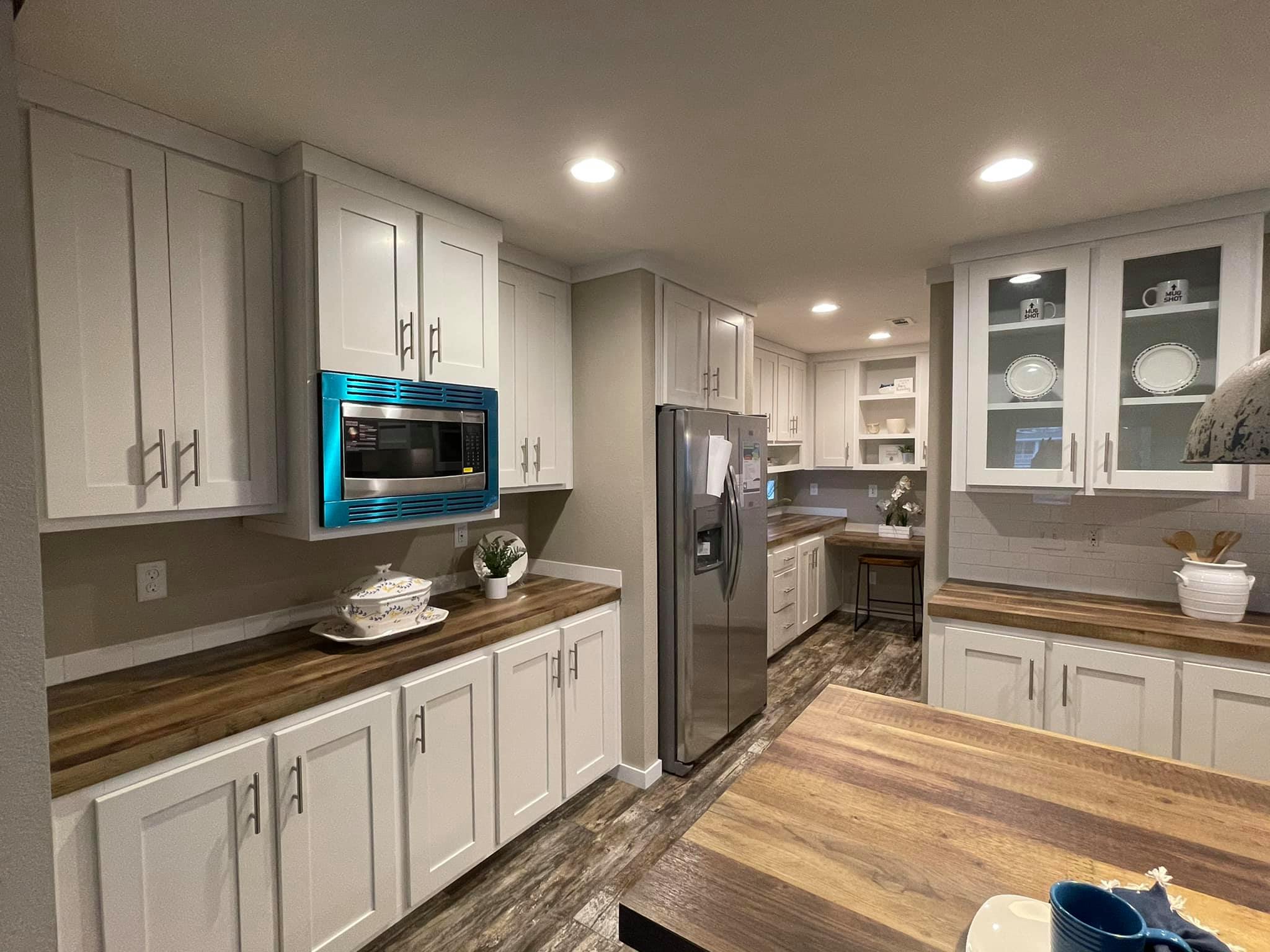 Modern kitchen with white cabinetry, wood countertops, and stainless steel appliances. Bright lighting and a cozy, organized ambiance.
