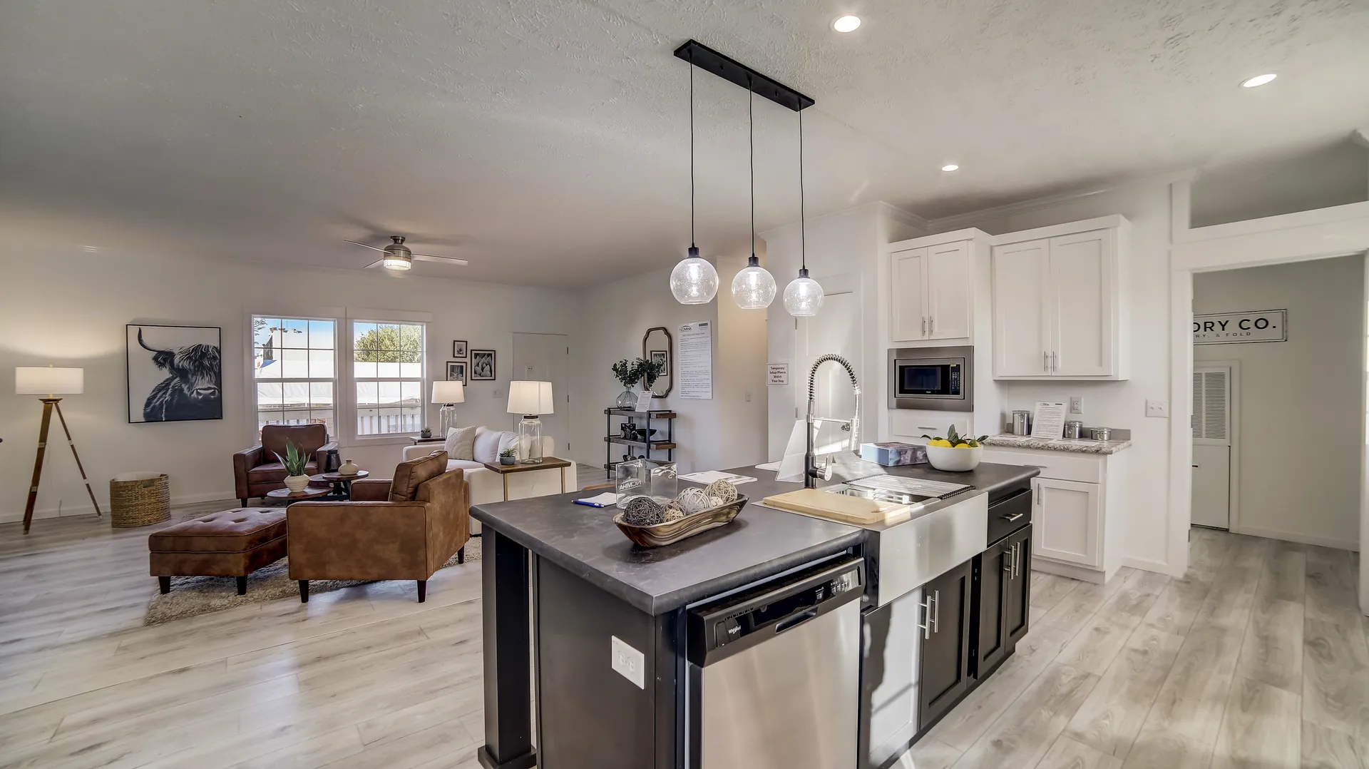 Modern, open living space with a kitchen island in the foreground. Brown leather sofa, large windows, and minimalistic decor create a cozy, inviting ambiance.