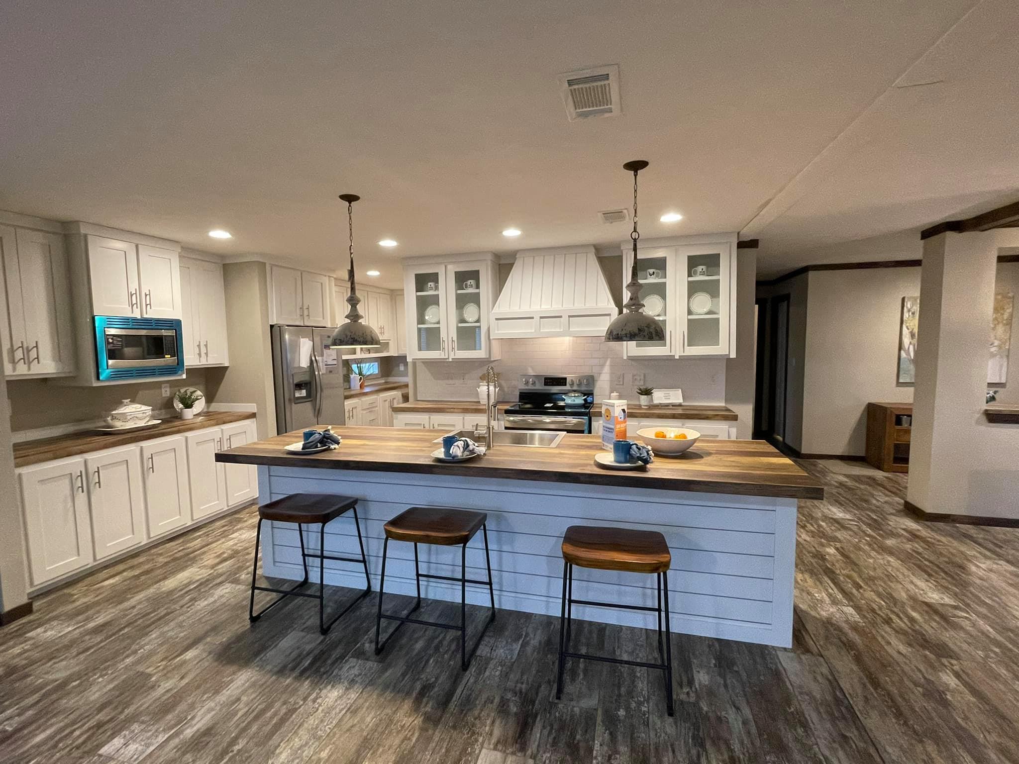 Spacious kitchen with a modern design, featuring a large island with stools, white cabinets, stainless steel appliances, and pendant lights, creating a cozy ambiance.