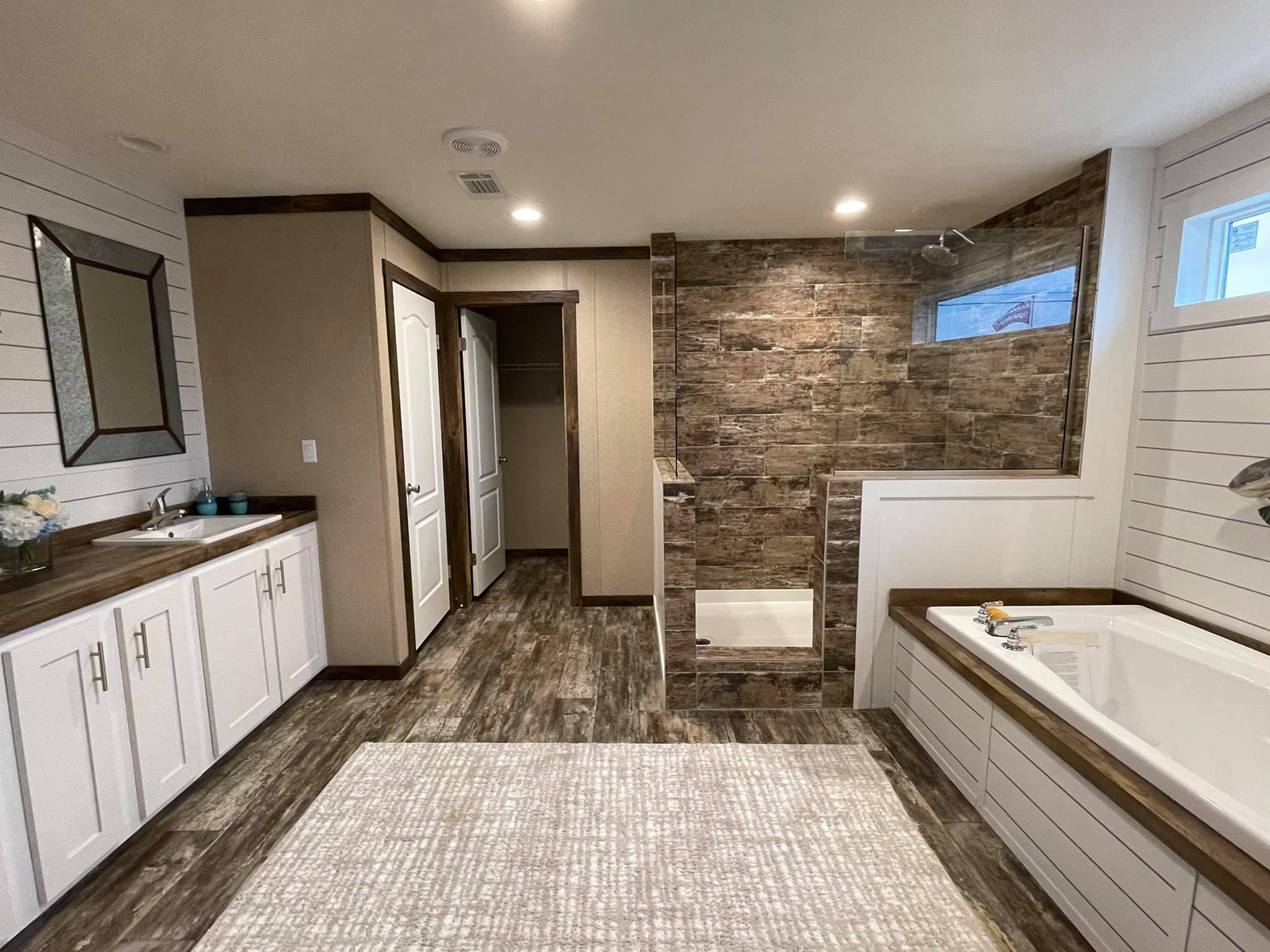 Spacious bathroom with wood floors, stone-tiled shower, dual sinks, tub, and white cabinetry. Bright light and neutral tones create a calm ambiance.