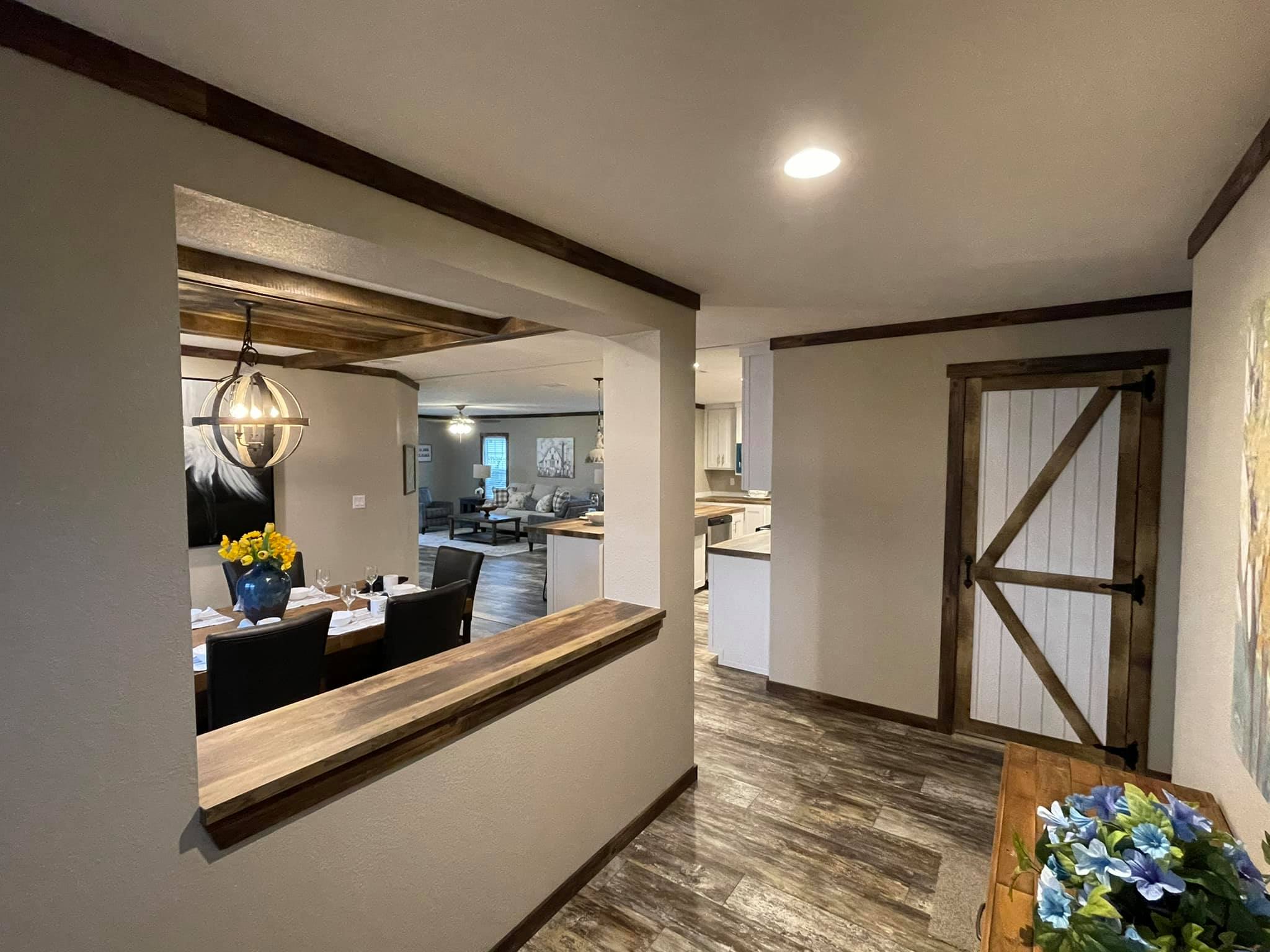 Modern farmhouse interior with rustic accents. Features include wooden floors, barn door, dining area with flowers, and soft lighting. Cozy and inviting ambiance.