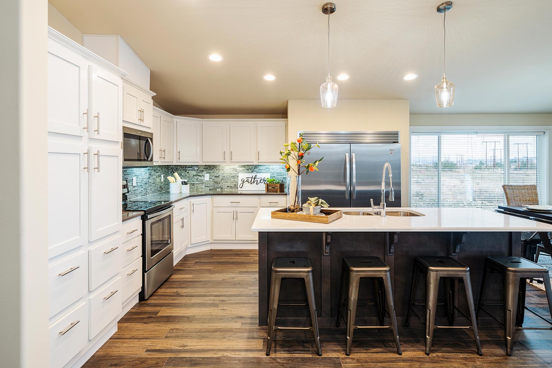 Modern kitchen with white cabinets and stainless steel appliances. A large island with bar stools, pendant lights, and a decorative vase adds elegance. Cozy and inviting atmosphere.
