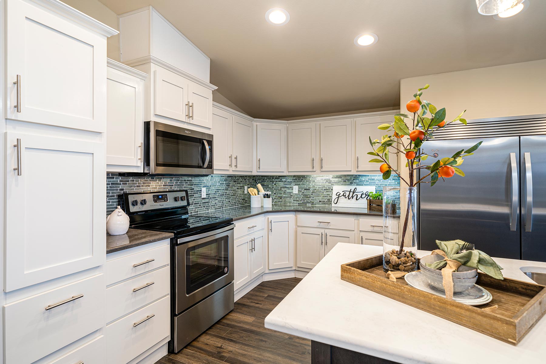 Modern kitchen with white cabinets, stainless steel appliances, and green tile backsplash. A wooden tray with decor sits on a white island, adding warmth.