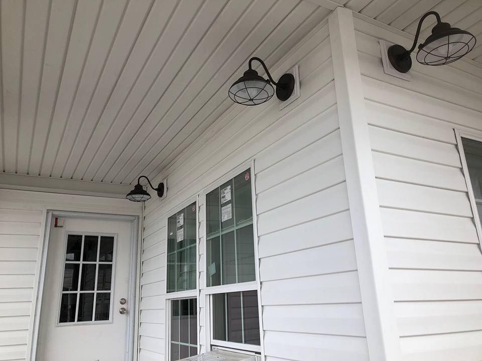 White house exterior with horizontal siding, three rustic metal lanterns, and a glass-paneled door. Two large windows offer a clean, modern look.