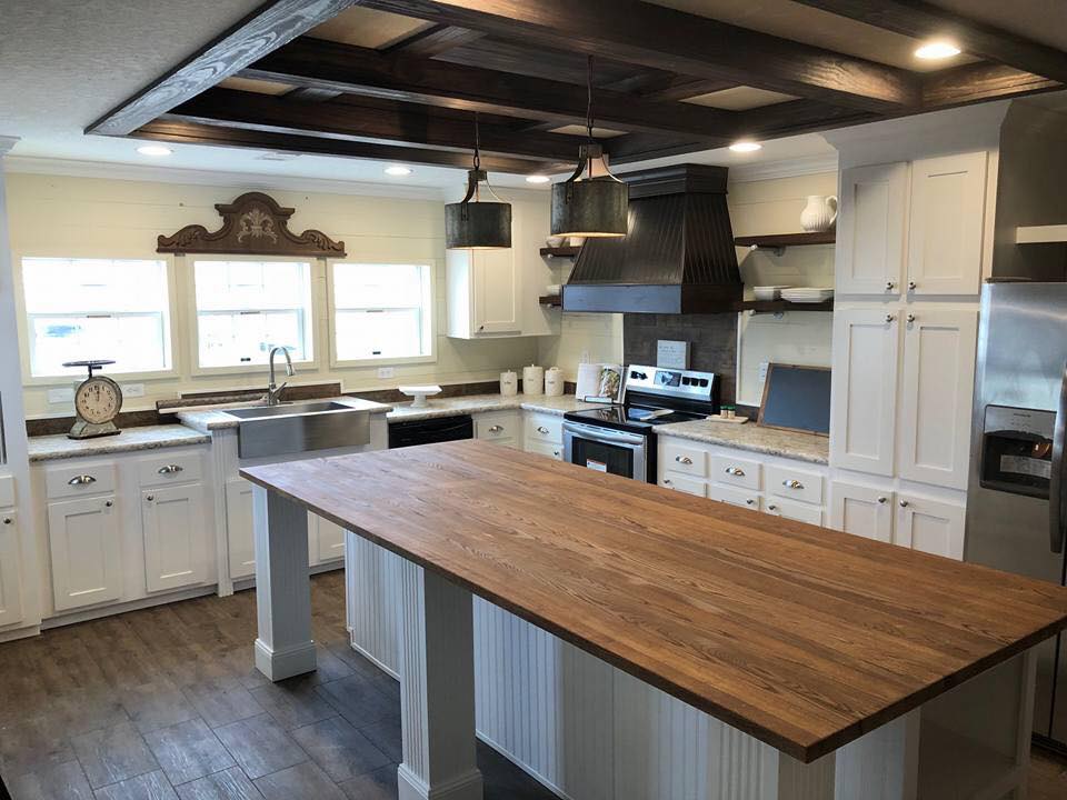 Spacious kitchen with wood island, white cabinets, and stainless steel appliances. Pendant lights hang above. Natural light from three windows creates a warm ambiance.