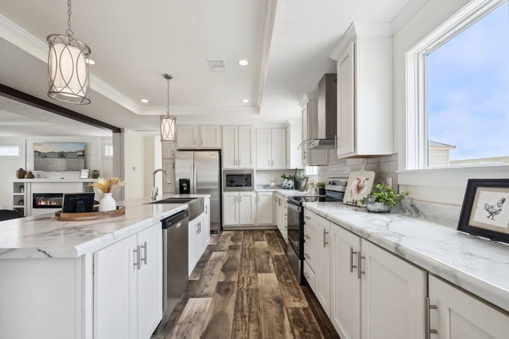 Modern kitchen with white cabinets, marble countertops, and wood flooring. Stainless steel appliances and pendant lights create a sleek, airy feel.