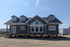 A modern gray house on stilts with three dormer windows and large central windows under a clear blue sky, conveying a sense of new beginnings.