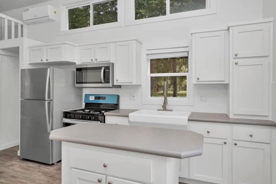 Modern kitchen with white cabinets, stainless steel appliances, and a farmhouse sink. Natural light through upper windows creates a bright, inviting ambiance.