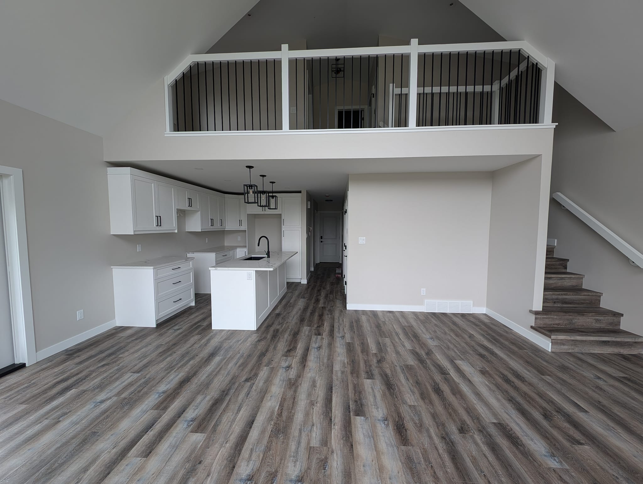 Spacious modern interior with high ceilings and loft. Features an open kitchen with white cabinets, island, pendant lights, and wooden floors.