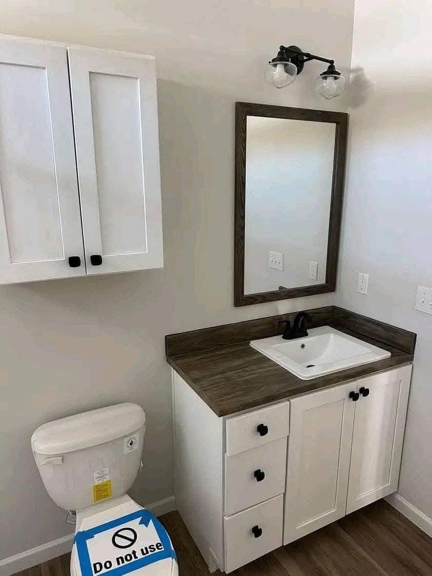 Bathroom with a wooden countertop, white vanity, and black fixtures. A "do not use" sign is on the toilet. Wall cabinet and mirror above vanity.