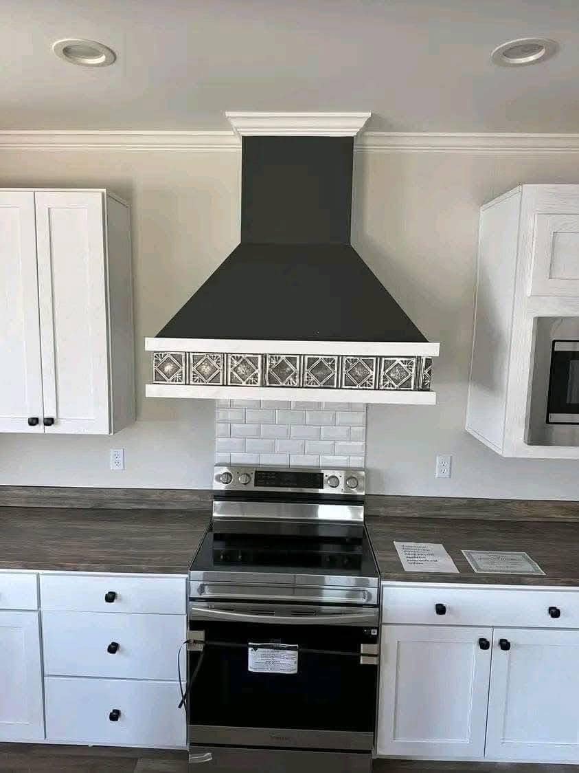 Modern kitchen interior with a black and white tiled range hood, stainless steel stove, white cabinets, and dark countertops, conveying a sleek and contemporary feel.