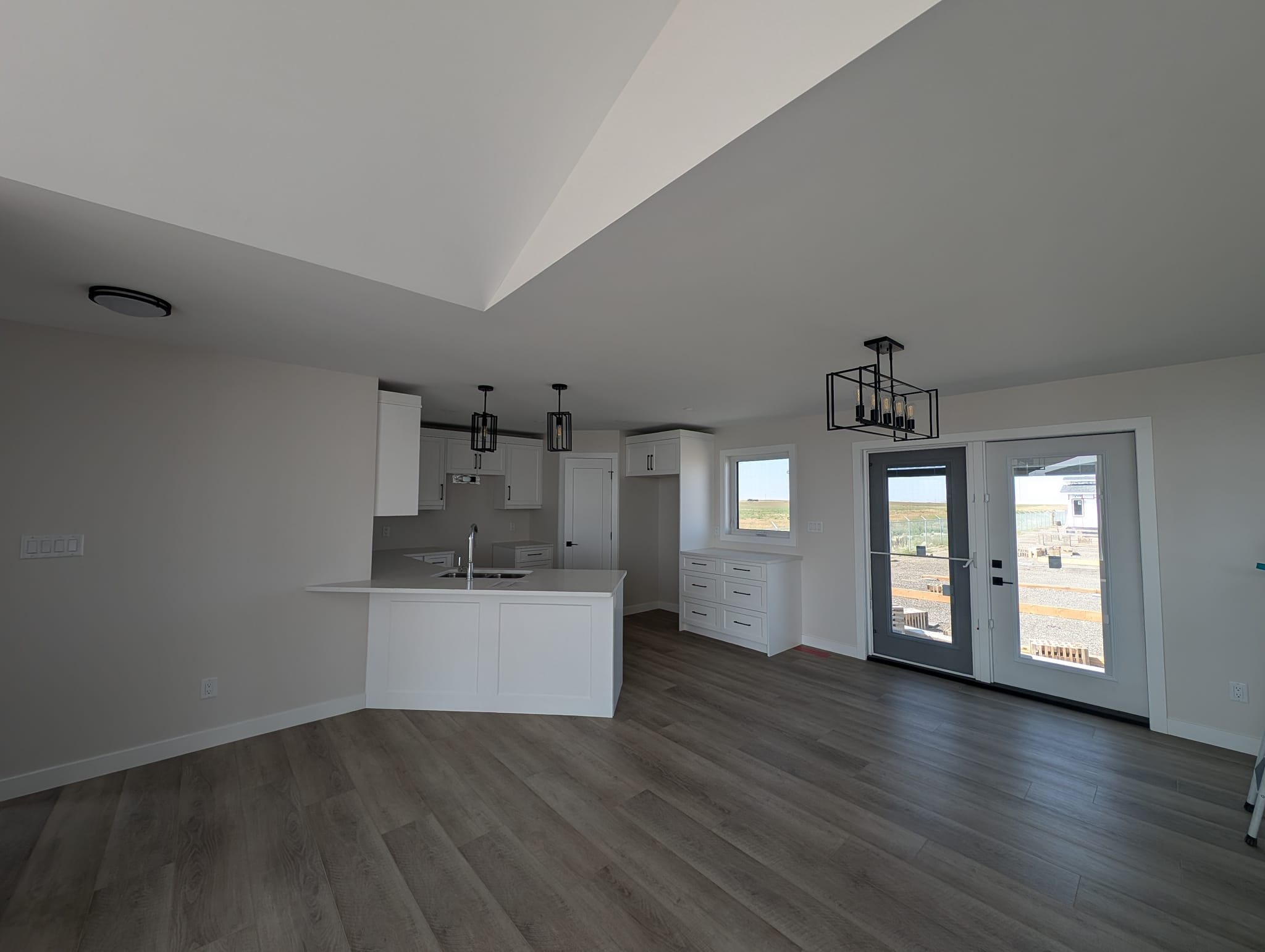 Spacious, bright room with white walls, large windows, and light wood flooring. Features a modern kitchen island and pendant lights, offering an open, airy feel.