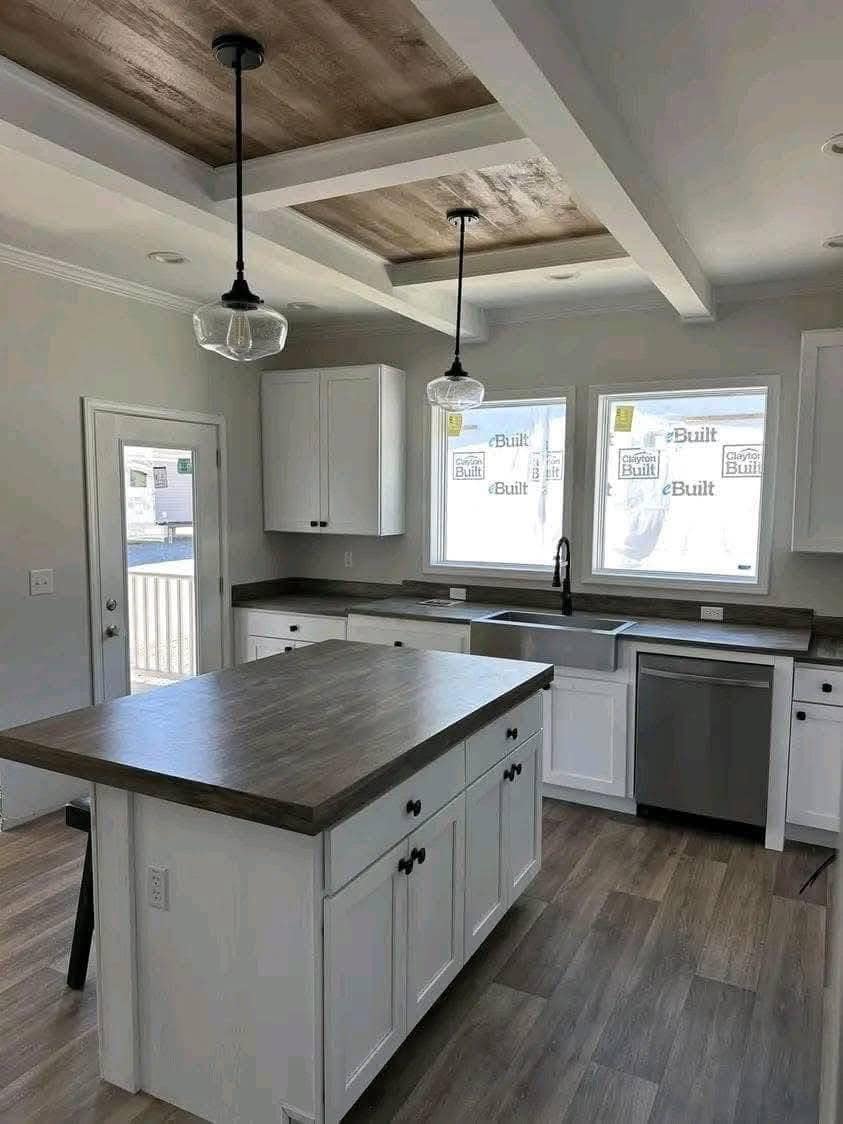 Contemporary kitchen with white cabinets, dark wood countertops, and a center island. Pendant lights hang from a coffered ceiling, creating a modern feel.